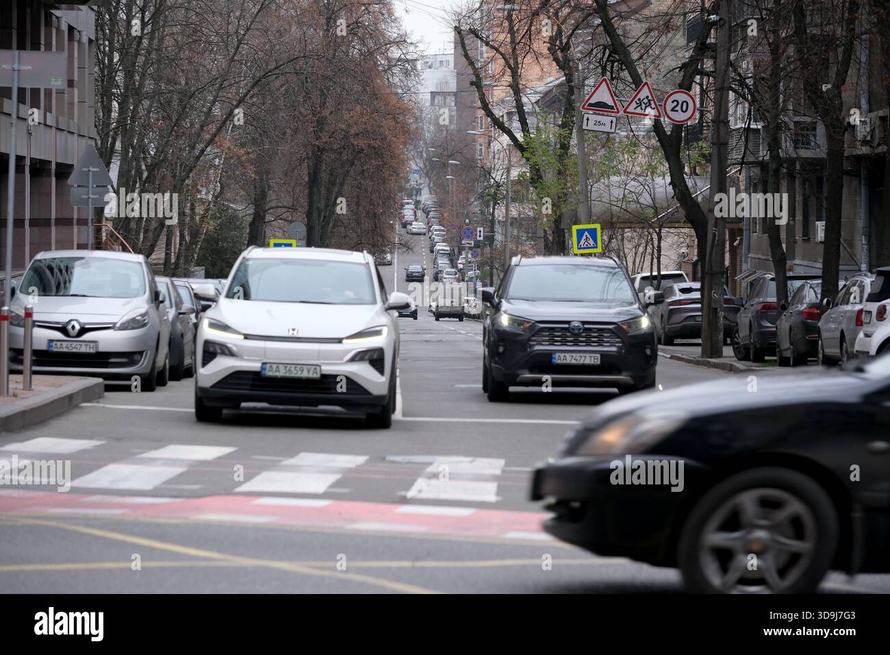 Zwei Autos nähern sich tagsüber einem Fußgängerübergang in einer lebhaften Stadt. Kiew, Ukraine. Dezember 2025. Stockfoto