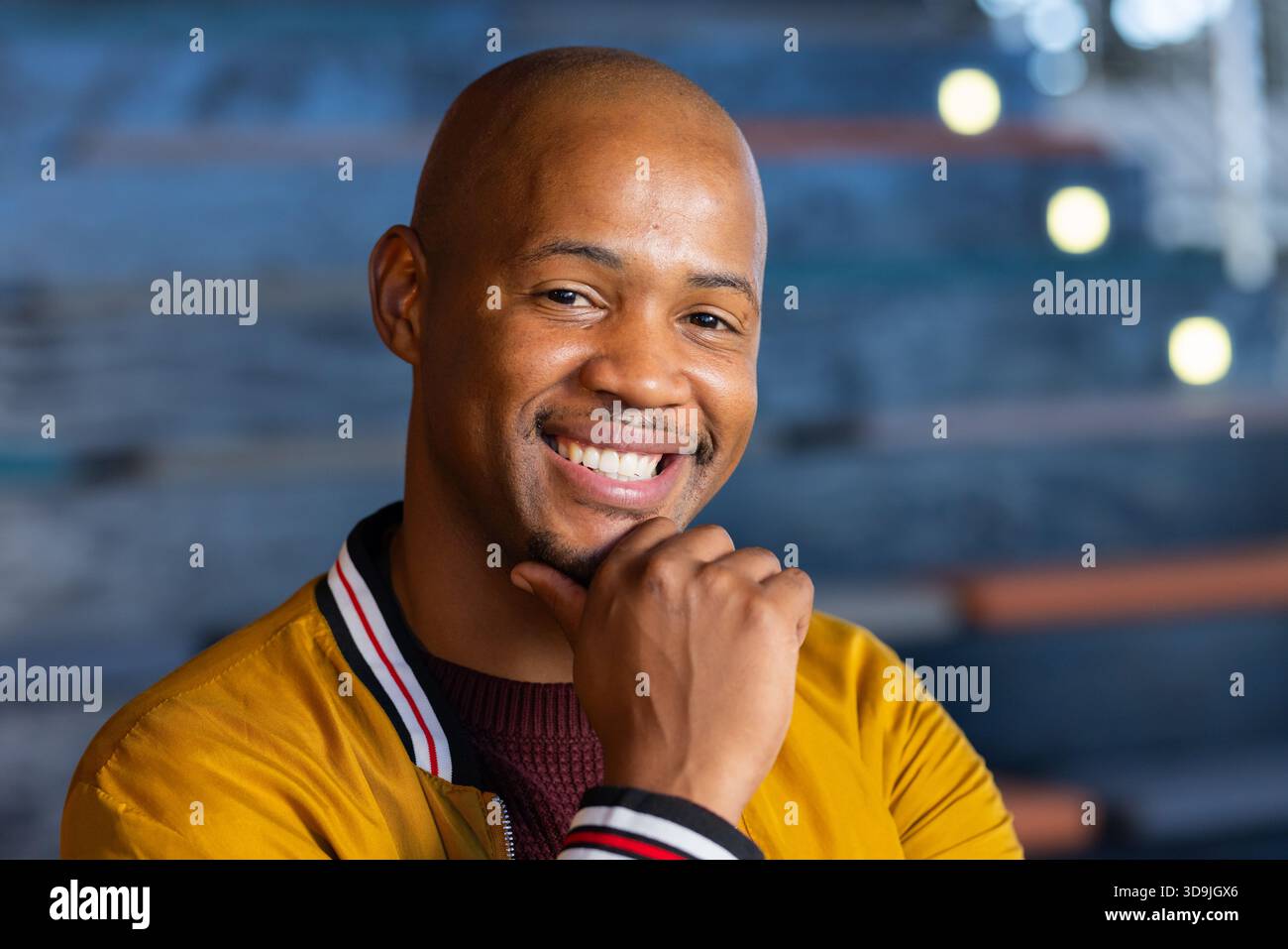 Afroamerikaner lächelnd, liegendes Kinn in der Café-Lounge mit Lichterketten in Bomberjacke Stockfoto