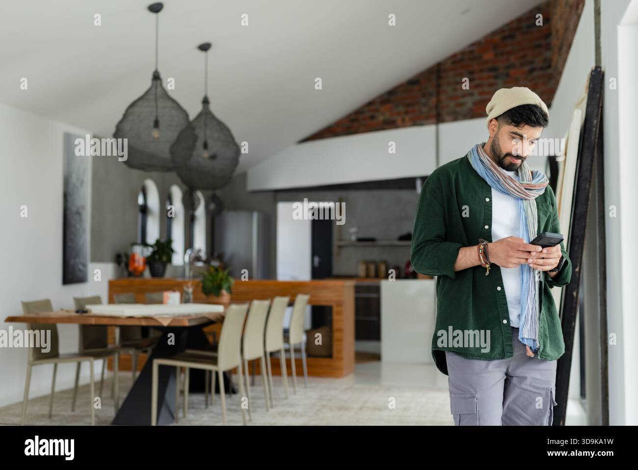 Indischer Mann, der das Smartphone zu Hause am Tisch hält, unter Hängeleuchten, Kopierraum Stockfoto