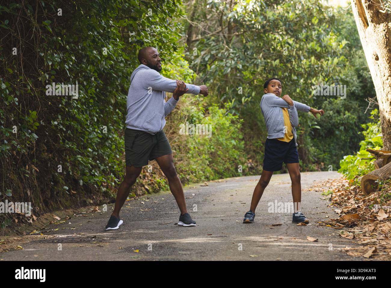 Afroamerikaner Vater und Sohn Strecken Arme auf gepflasterten Waldwegen in sportlichen Schuhen Stockfoto