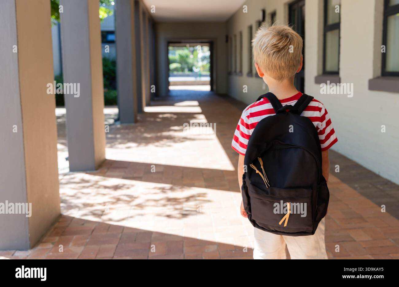 Schwarzer Rucksack, der an einer hellen Wand im überdachten Schulflur ruht und baumförmige Schatten wirft Stockfoto
