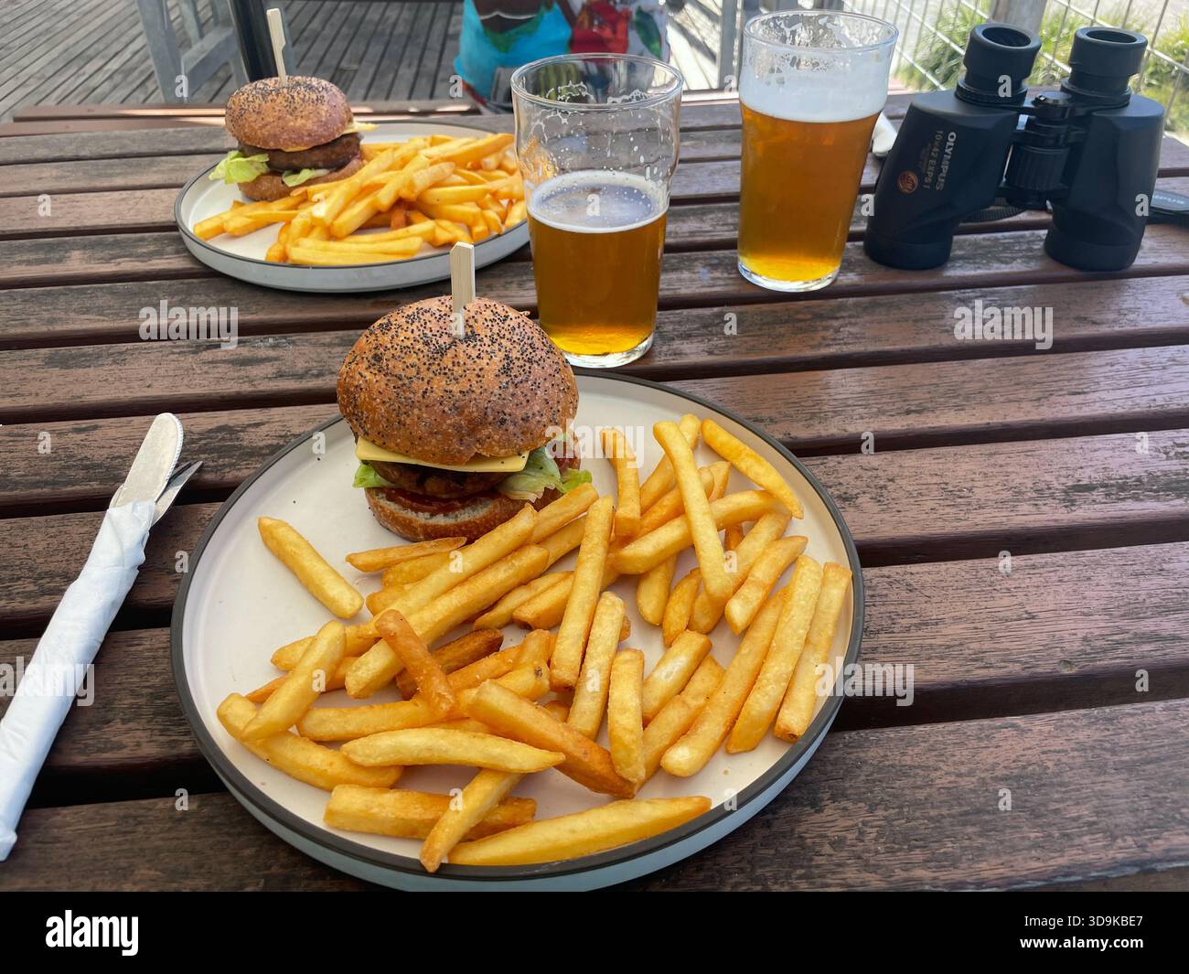Ein zwangloses Mittagessen im Freien auf einem Holztisch mit veganen Burgern, Pommes Frites, Bier und Ferngläsern. Wye Beach Hotel, Great Ocean Road, Australien - Smartphone-aufgenommenes Stockfoto