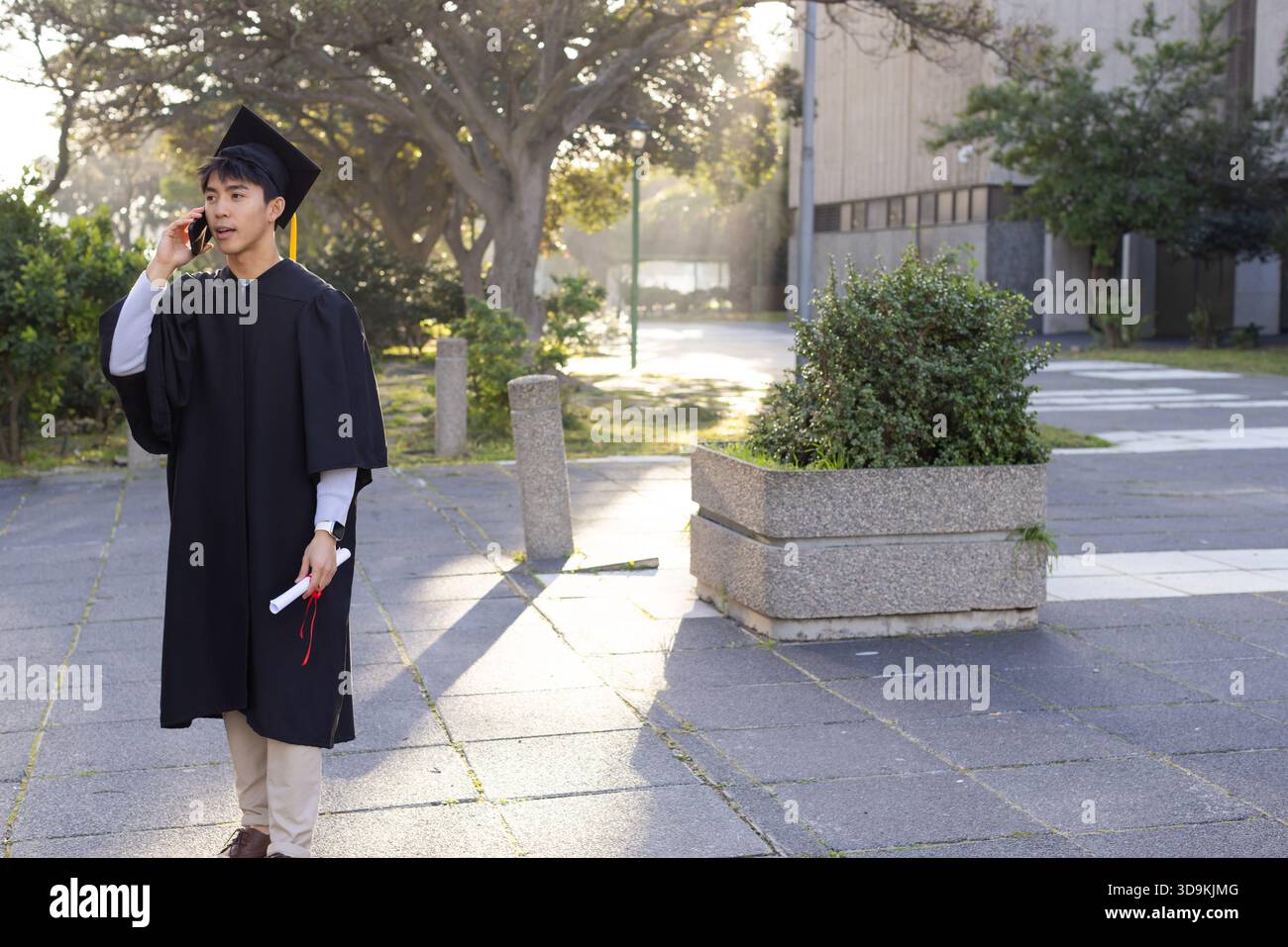 Asiatischer Mann posiert auf einem Quad, trägt eine Mütze mit Band-Diplom und spricht am Telefon, Kopierraum Stockfoto