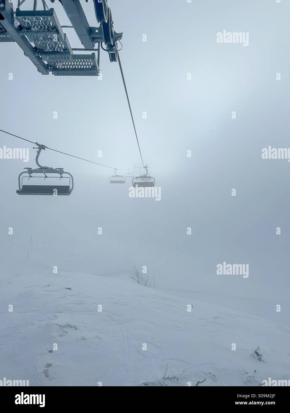 Eine schneebedeckte Winterszene auf dem Jahorina-Berg mit einem Skisessellift, der durch dichten Nebel auftaucht und eine ruhige und stimmungsvolle alpine Landschaft schafft. - Smartphone-aufgenommenes Stockfoto