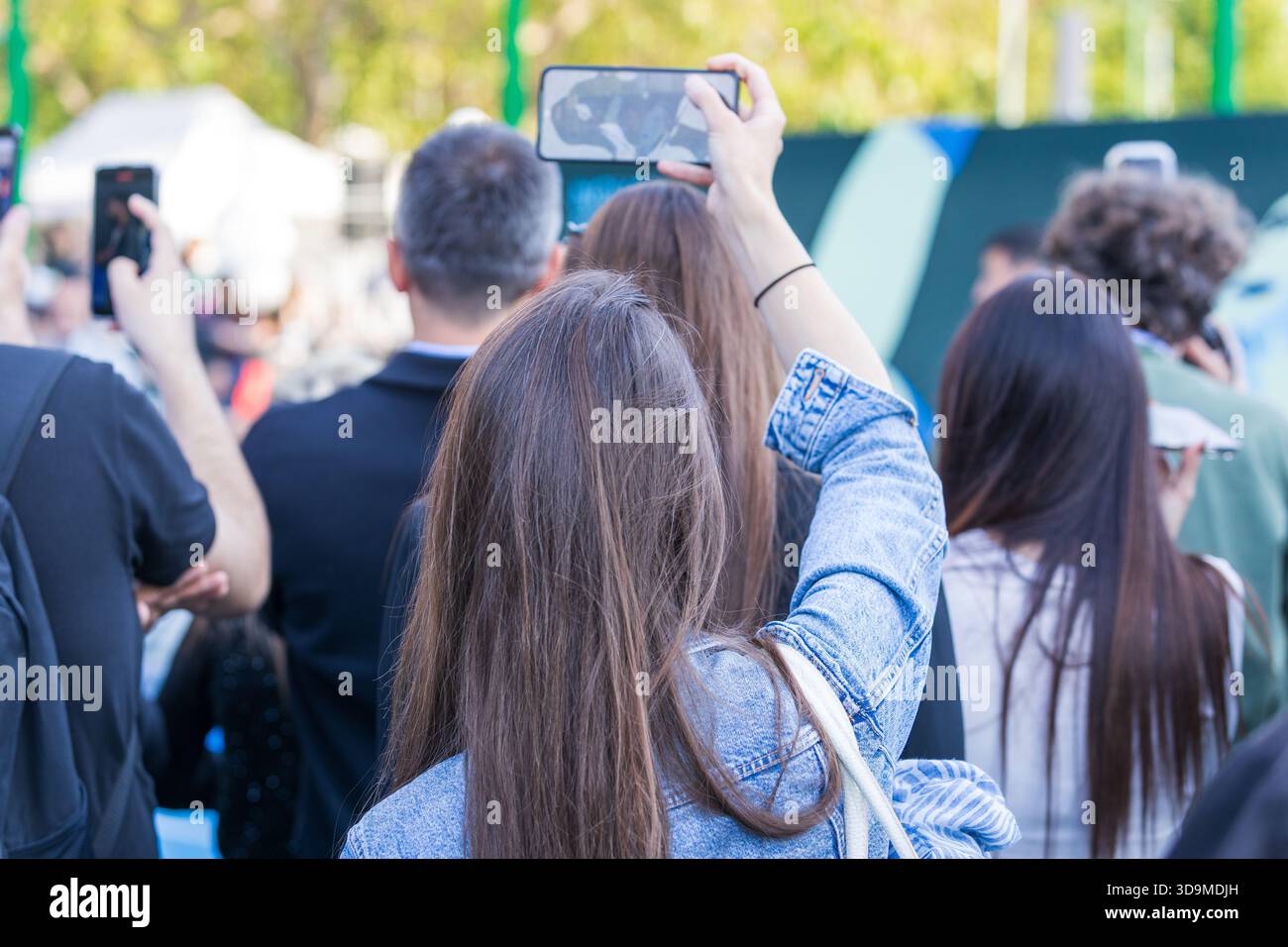 Eine vielfältige Gruppe von Personen, die an einer öffentlichen Veranstaltung im Freien teilnehmen und den Moment mit Smartphones festhalten. Das Bild spiegelt moderne digitale Kultur wider, soziale Stockfoto