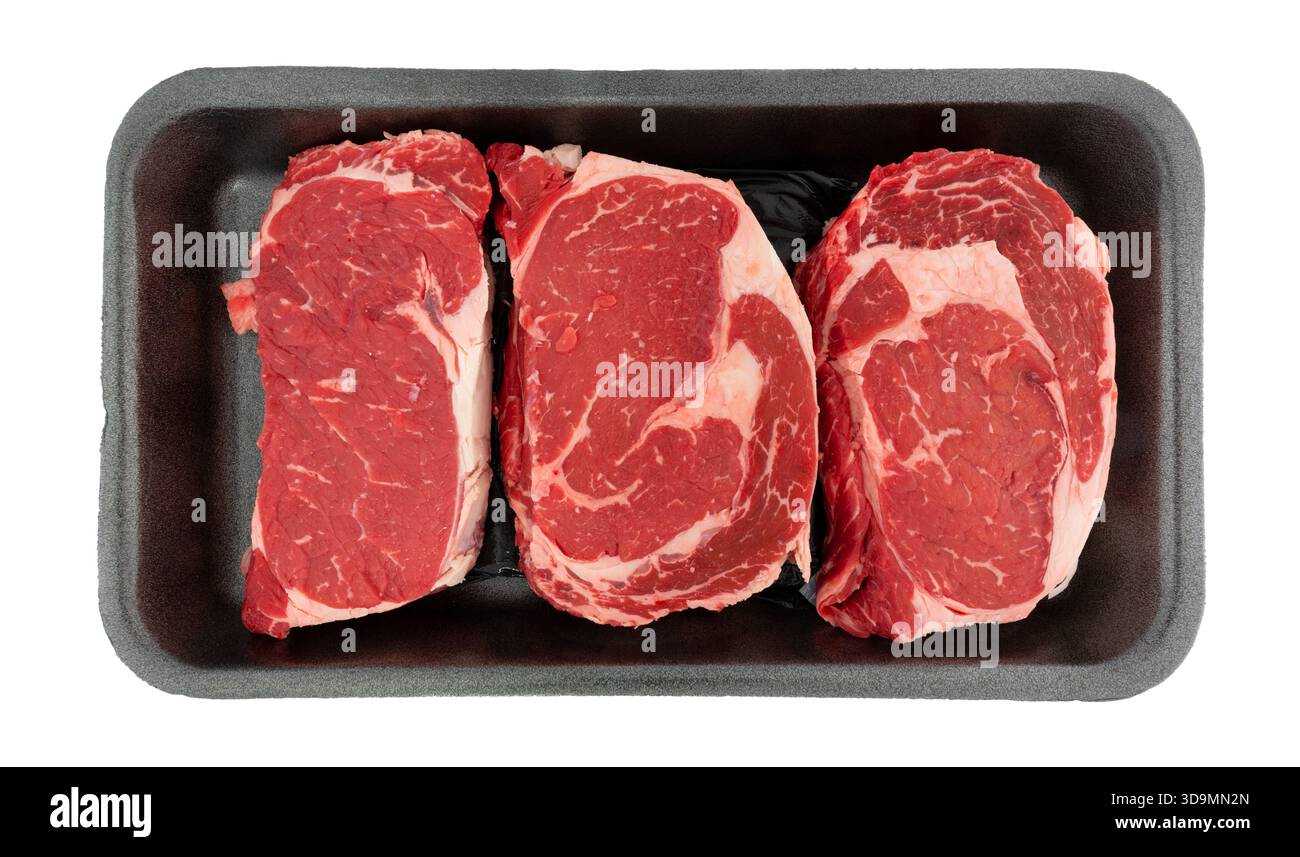 Blick von oben auf drei Ribeye-Steaks in einem schwarzen Schaum-Fleischtablett auf weißem Hintergrund. Stockfoto