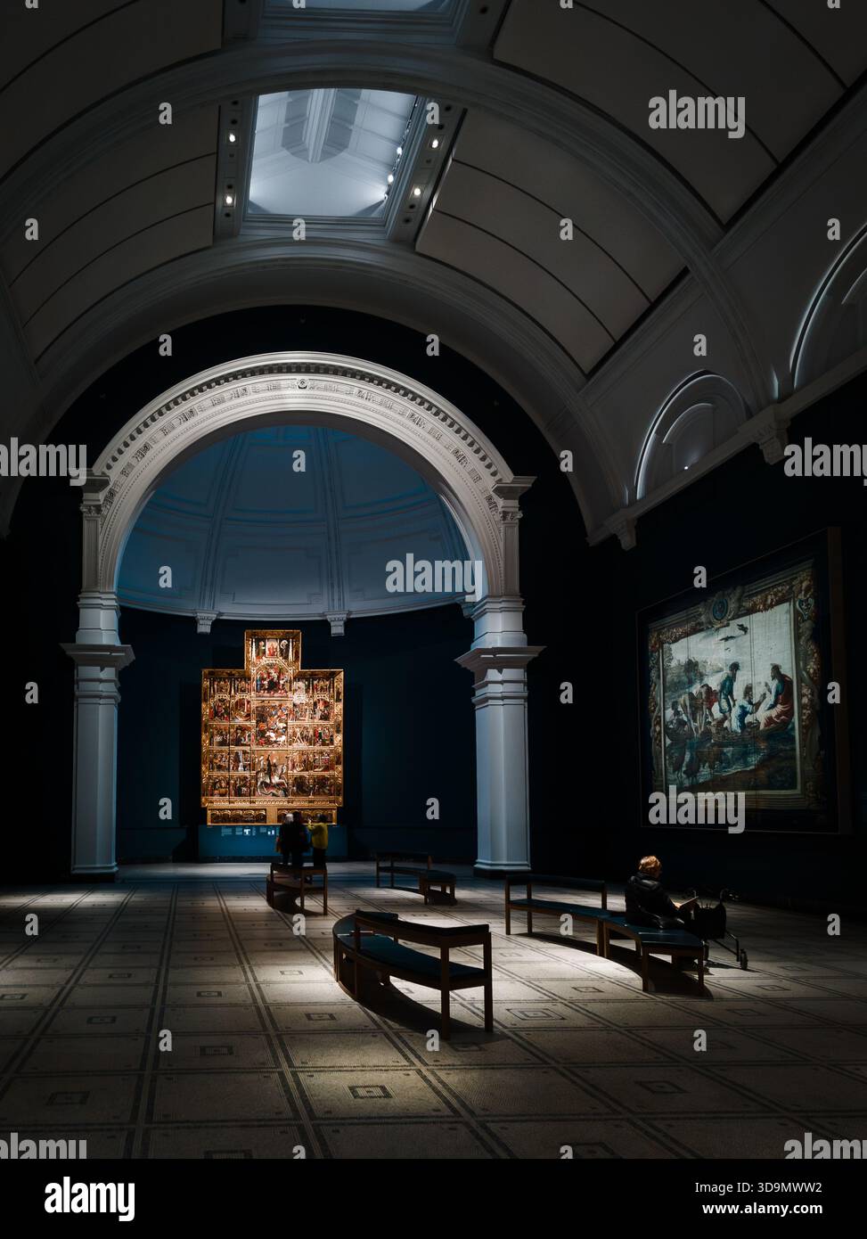 Dramatisches Inneres des V&A Museums mit beleuchtetem Altar, großen architektonischen Bögen und Besuchern, die sich zwischen sanft beleuchteten Galeriebänken befinden Stockfoto