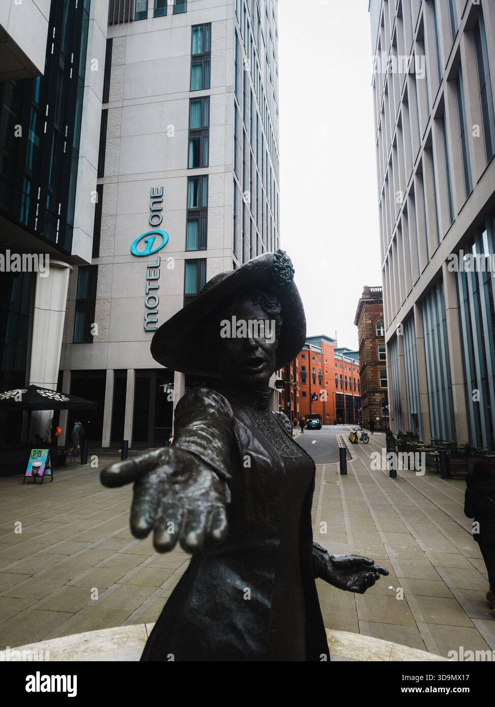 Bronzestatue einer Frau, die ihre Hand ausstreckt, zwischen modernen Hochhäusern in einer Straßenszene in Manchester mit urbaner Architektur und Fußgängerzone Stockfoto