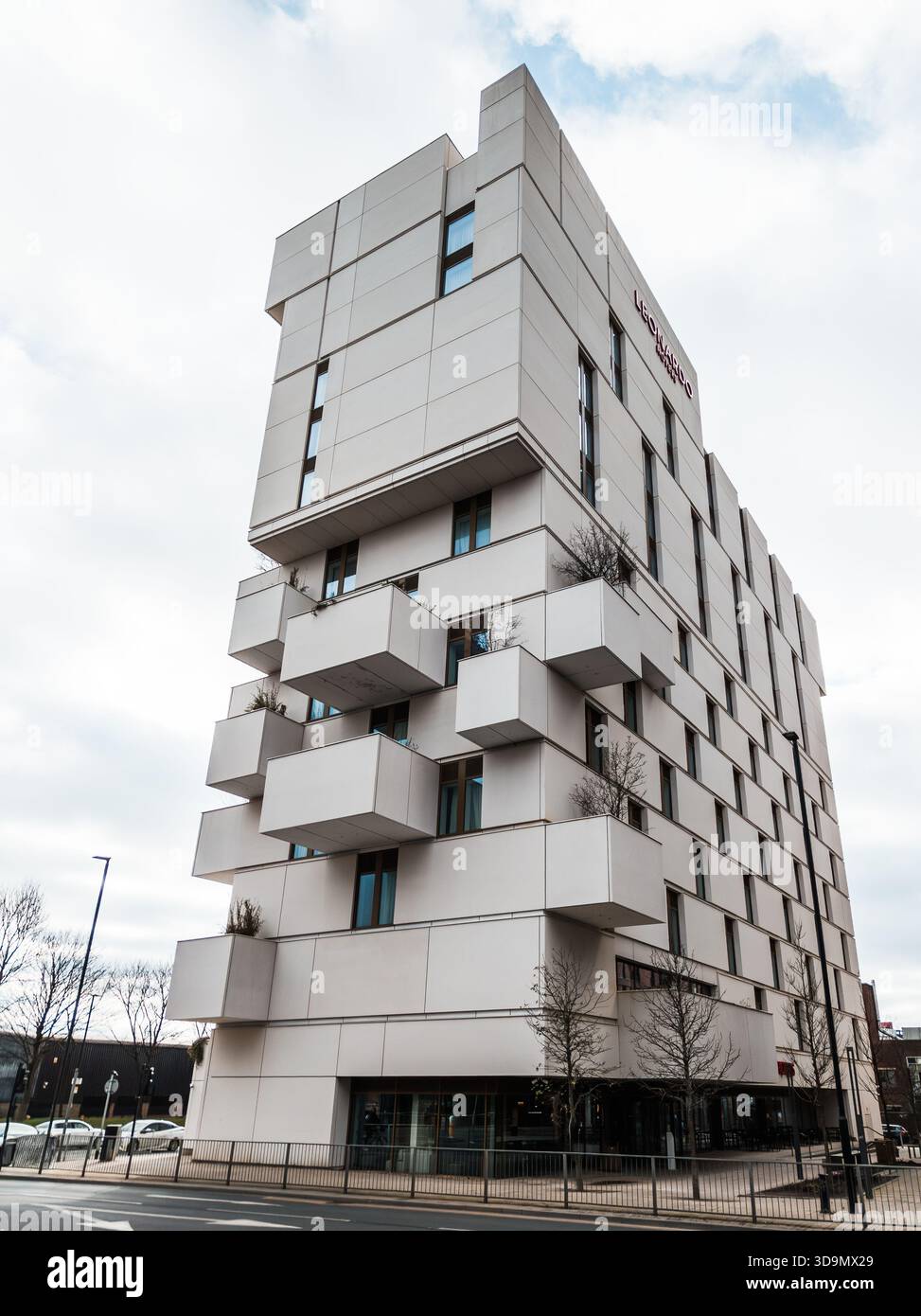 Beeindruckendes modernes Gebäude mit geometrisch abstehenden Balkonen und klaren architektonischen Linien, die sich in den Straßen von Manchester vor einem hellen Himmel erheben Stockfoto