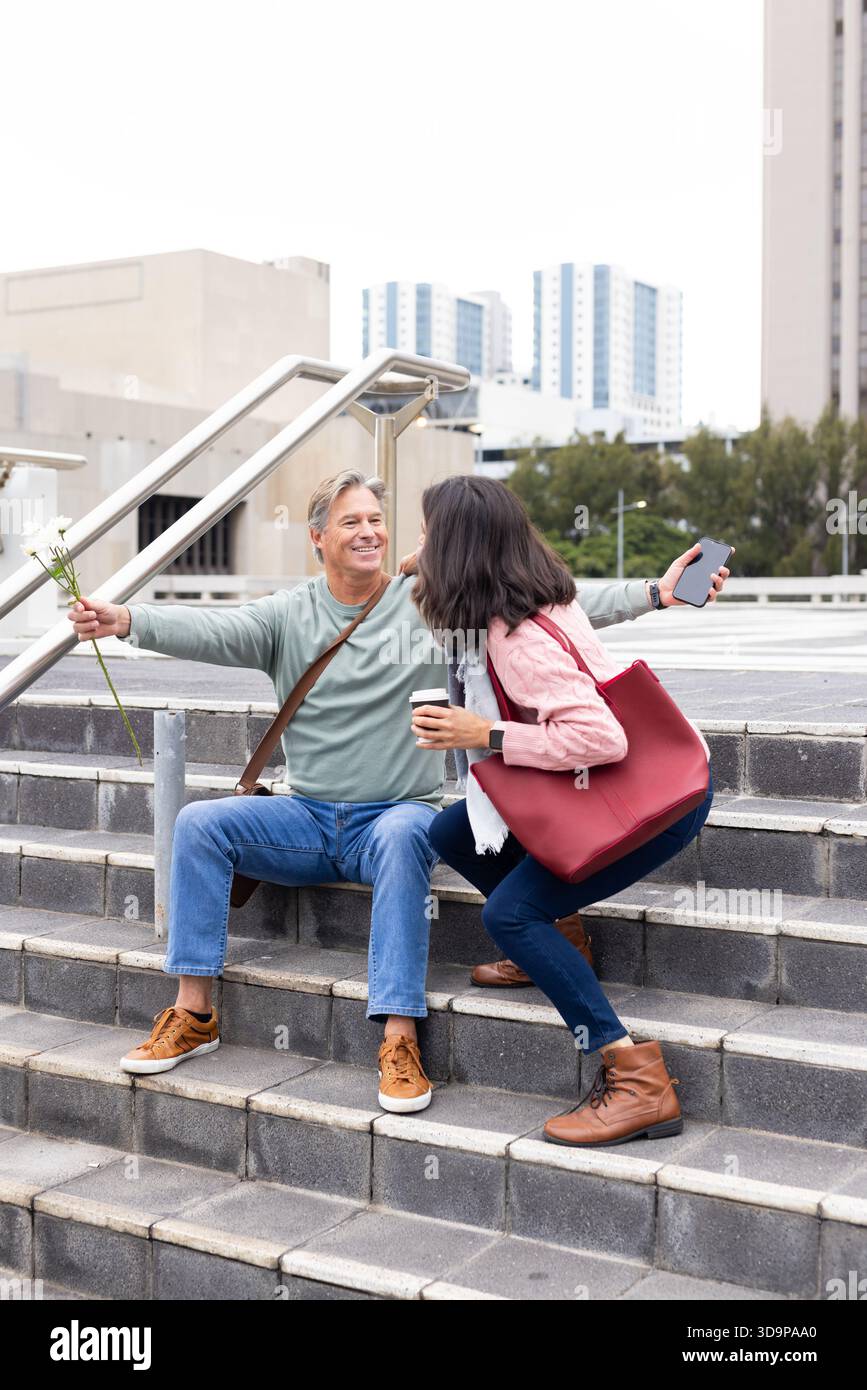 Verschiedene ältere Ehepaare interagieren auf plaza Steps, halten Kaffeetassen-Smartphone und weiße Blumen Stockfoto