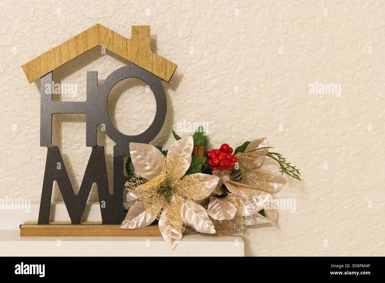 Ein hölzernes Schild in der Form eines Hauses zeigt das Wort „Zuhause“. Es befindet sich auf einem Regal mit dekorativen Blumen und Beeren in der Nähe Stockfoto