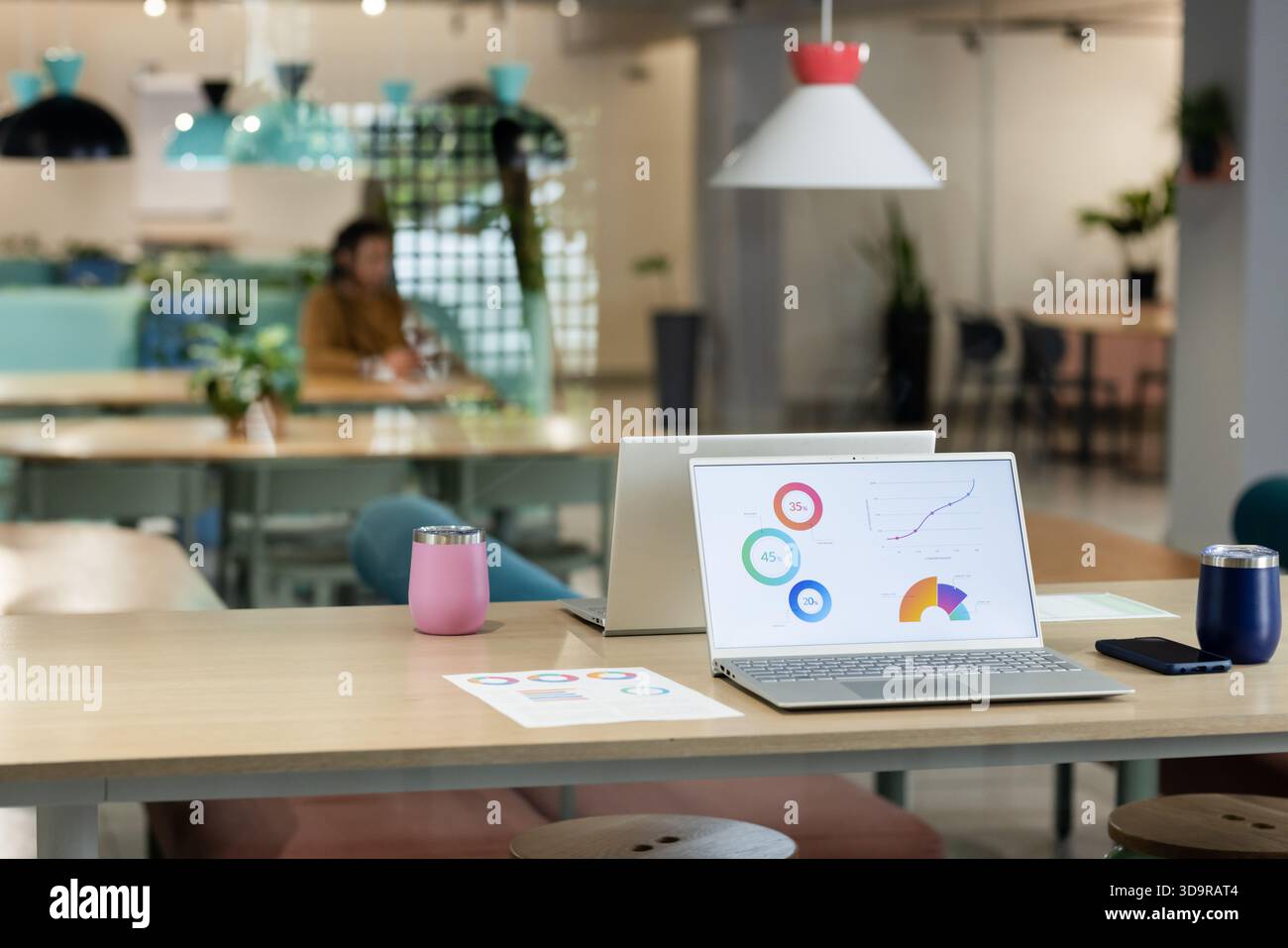 Der offene silberne Laptop zeigt Karten und Grafiken auf einem Holztisch mit rosafarbenen und marineblauen Gläsern Stockfoto