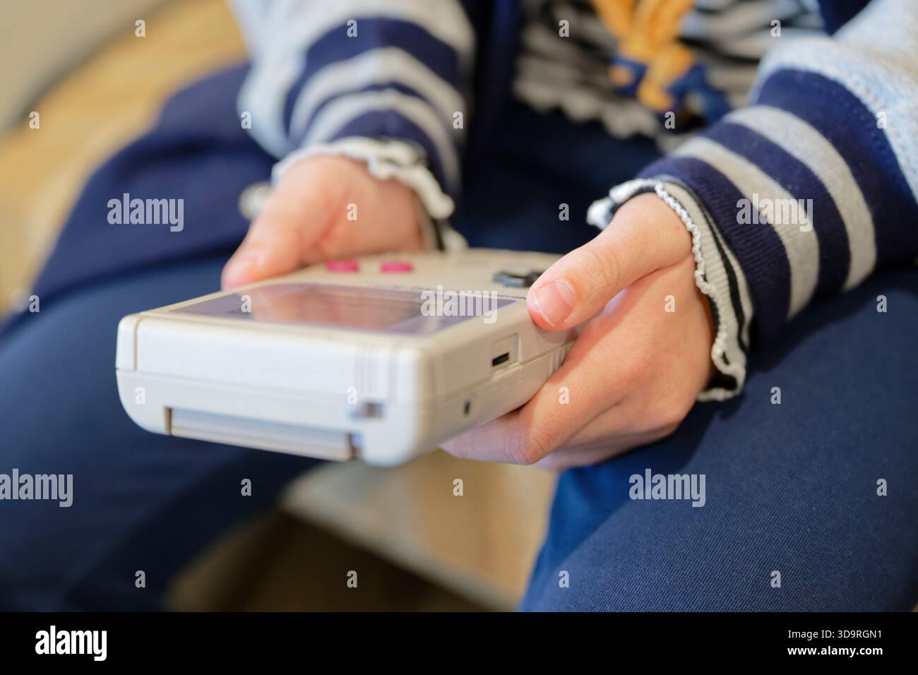 Die Hände einer Person, die eine Vintage-Handheld-Spielkonsole hält und die Tasten und den Bildschirm des Geräts zeigt. Der Hintergrund ist leicht verschwommen und betont Stockfoto