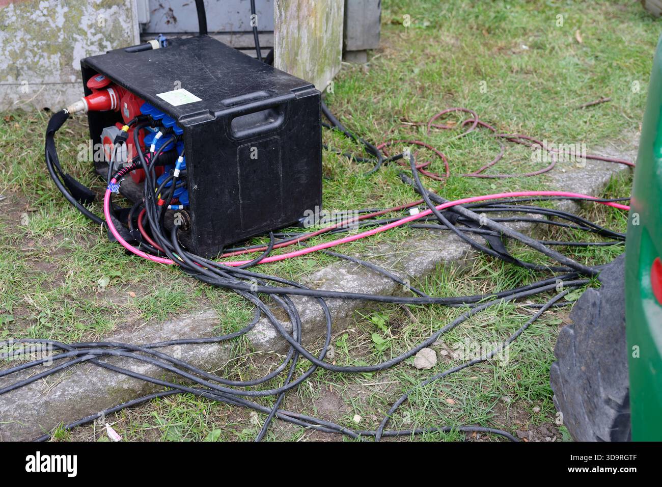 Ein schwarzer, tragbarer Stromverteiler mit mehreren Industriekabeln und Steckverbindern liegt auf einem grasbewachsenen Gebiet und liefert Strom für die Outdoor-Technologie Stockfoto
