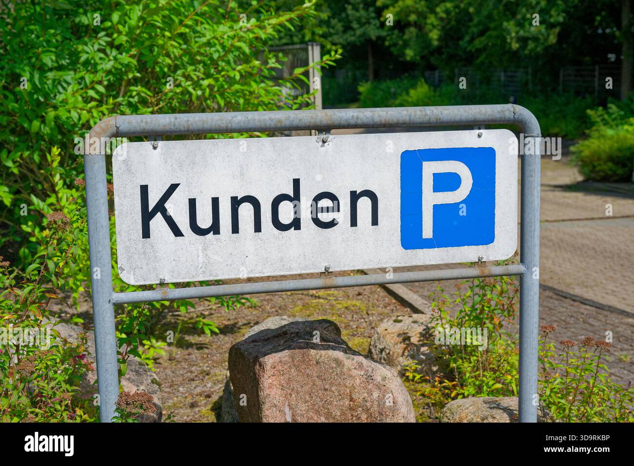 Ein Metallpfosten trägt ein weißes Kunden-Parkschild mit einem blauen P-Symbol, während ein großer Stein an der Basis aufliegt und einen einfachen, zweckmäßigen parki am Straßenrand bildet Stockfoto