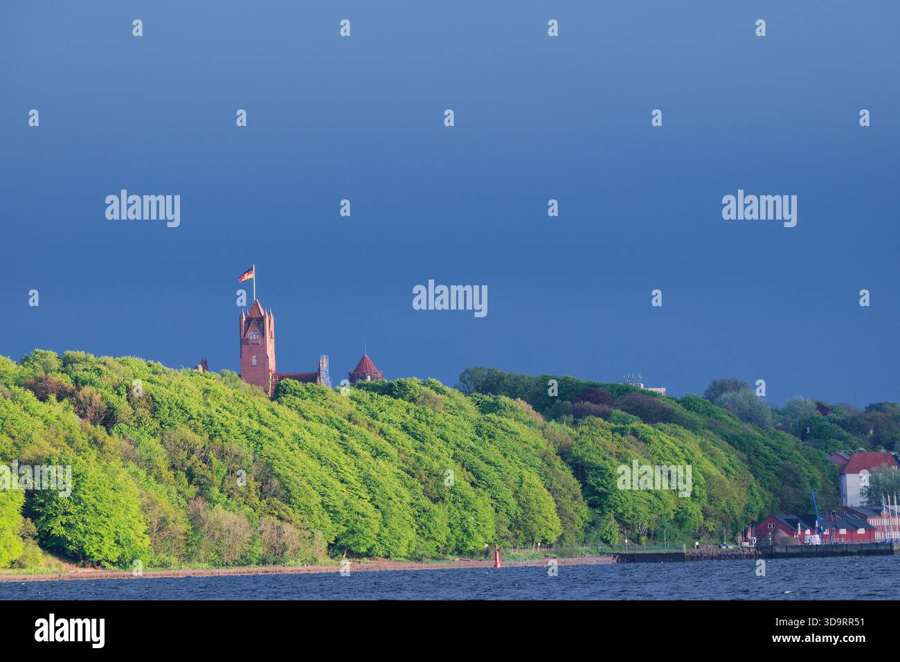 Filmische Aufnahmen des historischen Marineschulturms in Flensburg mit deutscher Flagge, grünem Wald und dramatischem grauem Himmel. Perfekt für Intros, Reise-cli Stockfoto
