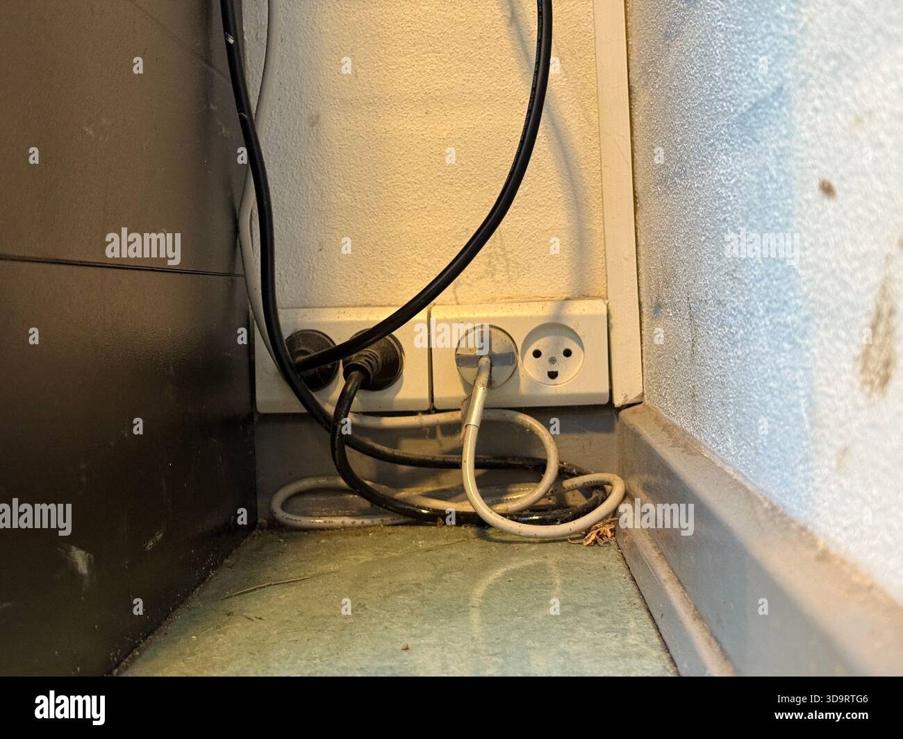 Unordentliche Stromkabel und Steckdosen in einer staubigen Ecke. Perfekt für die Darstellung von Energieverbrauch, elektrischer Sicherheit, Hauswartung oder Arbeit Stockfoto