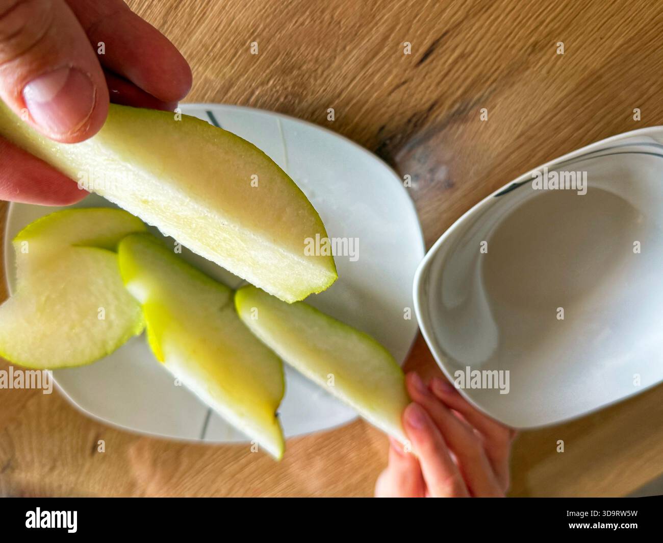 Ein weißer Teller hält ordentliche Birnenscheiben in einem weichen Fächer, helles Fleisch und klarer Saft fangen sanftes Licht auf und der kleine Snack lässt eine ruhige Pause vor sich Stockfoto