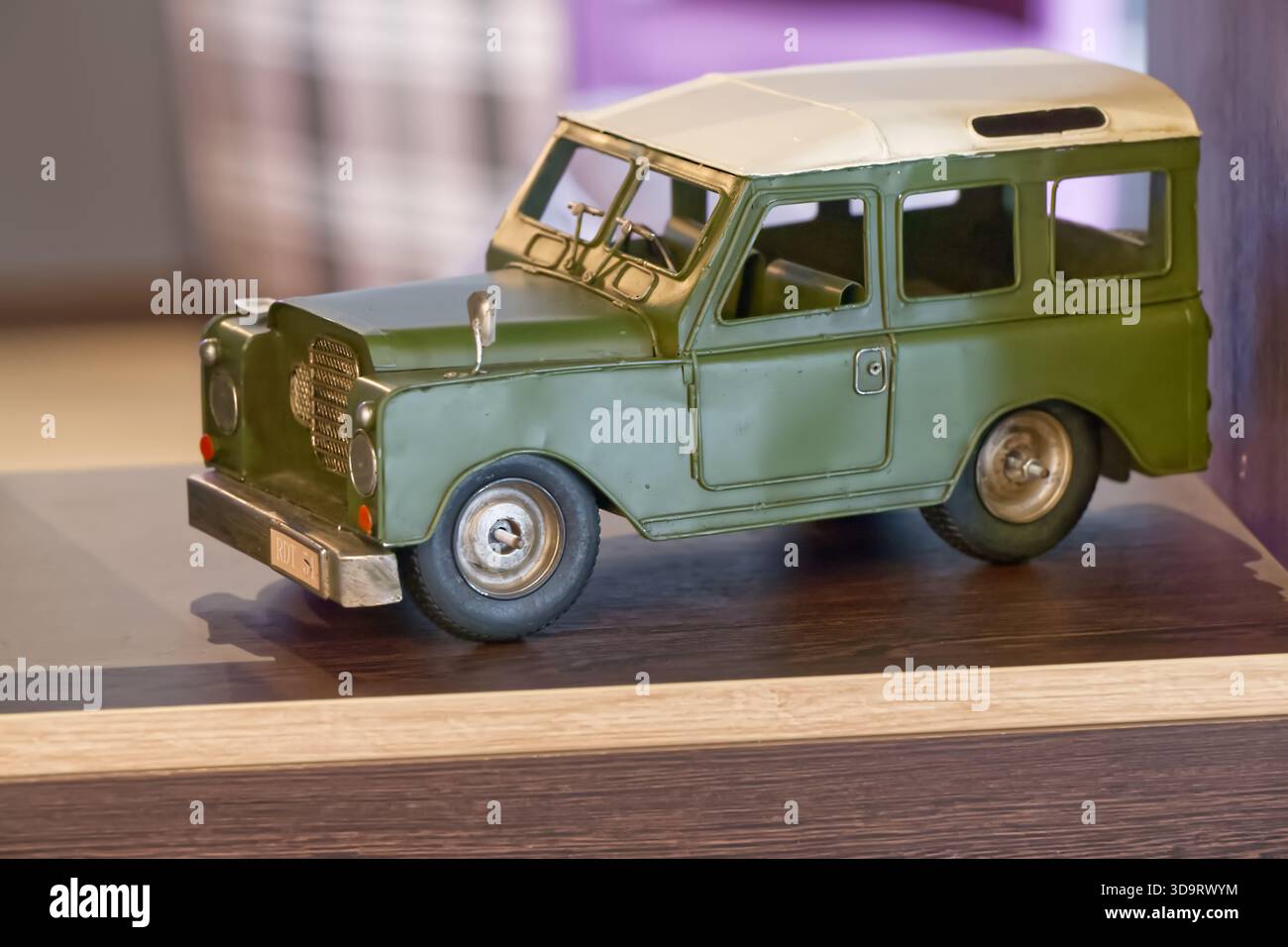 Ein Vintage-Spielzeugmodell eines grünen und cremefarbenen Autos, ausgestellt auf einer Holzoberfläche. Das Fahrzeug verfügt über detaillierte Räder und ein klassisches Design, das an Nein erinnert Stockfoto