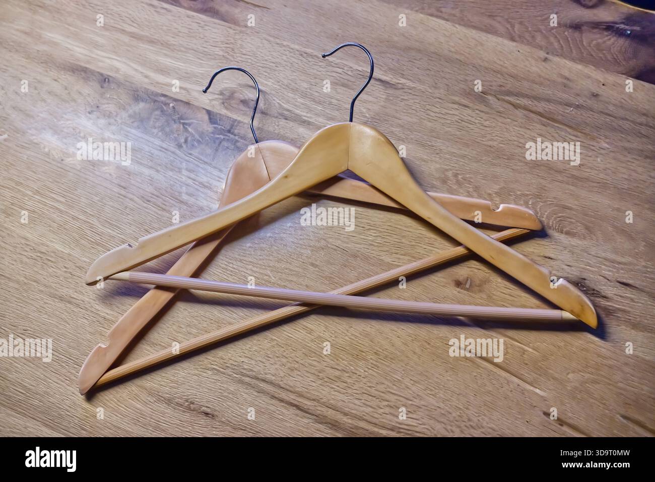 Zwei Holzbügel kreuzen sich auf einer Holztischoberfläche, die ihre glatte Oberfläche und ihre natürliche Farbe zeigen. Stockfoto