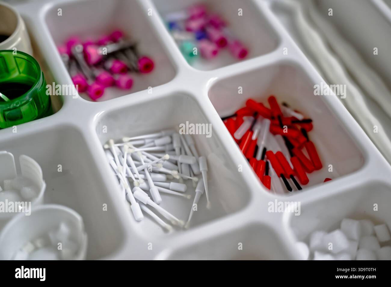 Eine Nahansicht eines abgeteilten Organizers, der mit verschiedenen kleinen Gegenständen gefüllt ist, einschließlich weißer und roter Anschlüsse, farbenfroher Stifte und anderen verschiedenen Artikeln Stockfoto