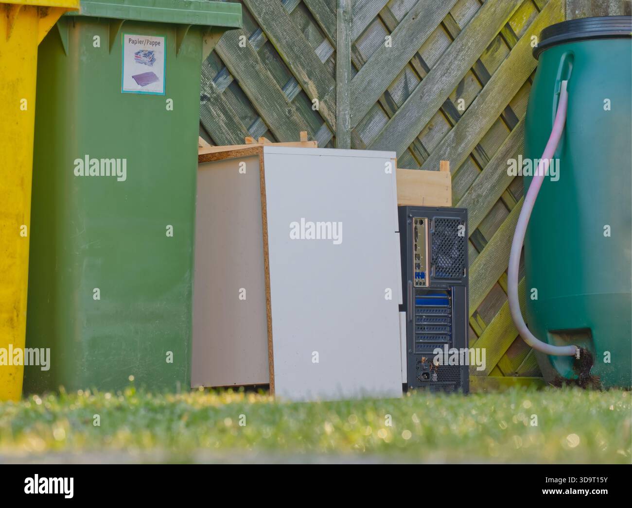Eine Szene mit einem grünen Recyclingbehälter, einem gelben Mülleimer und einem weißen Schrank neben einem Computerturm. Der Hintergrund ist ein hölzerner fe Stockfoto