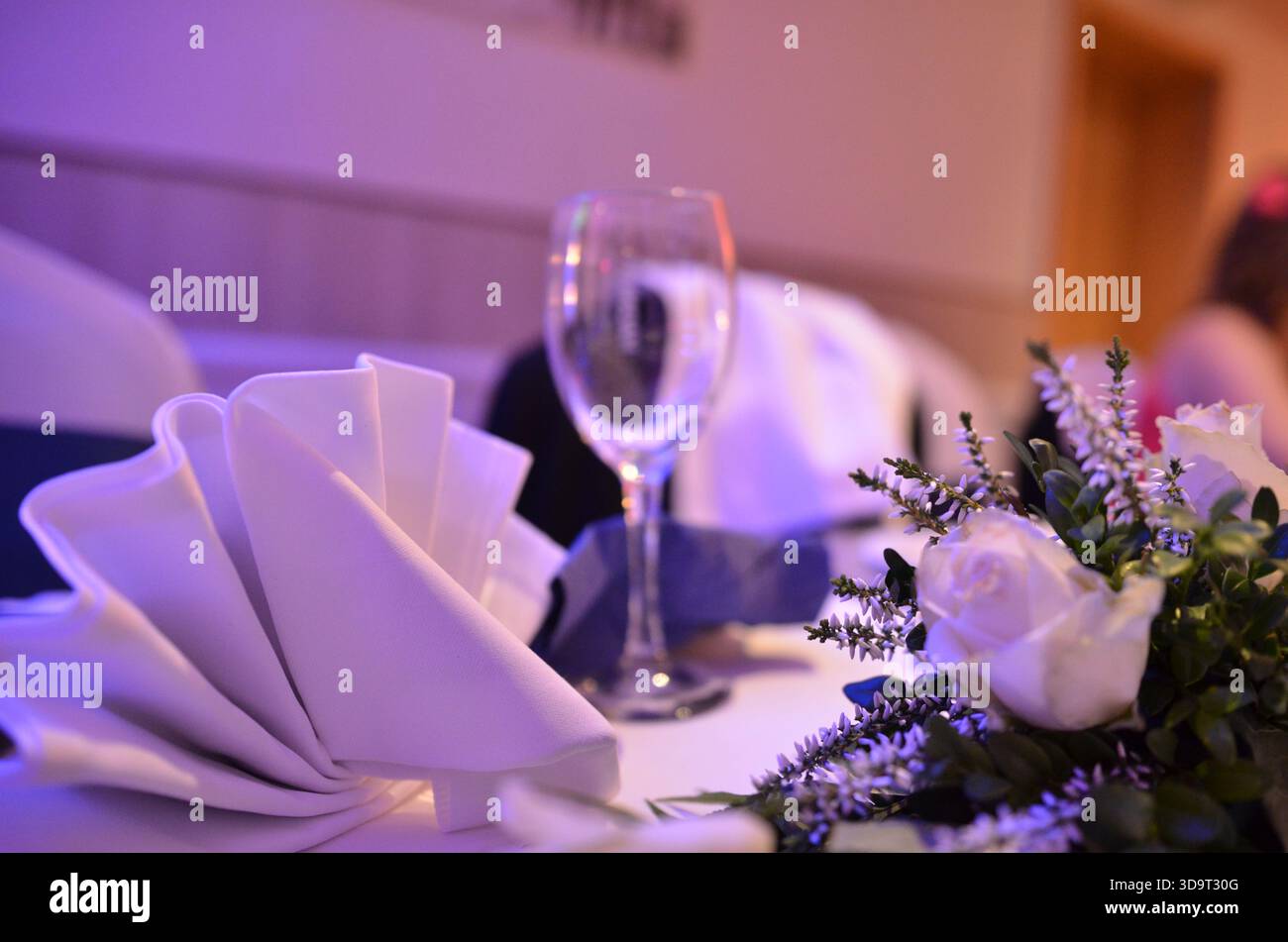 Ein wunderschön gestalteter Esstisch bei einer Hochzeit mit lila Deko und einem Sektglas zum Toasten, einer Leinenserviette und elegantem Besteck auf einem Holz Stockfoto