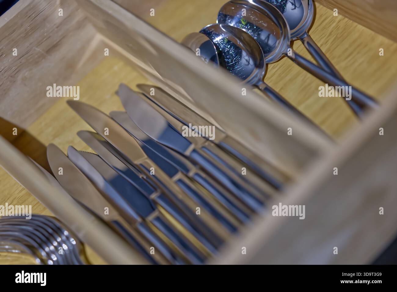 Eine hölzerne Besteckschublade mit ordentlich angeordneten Messern und Löffeln aus Edelstahl. In der Schublade befindet sich ein sauberes und organisiertes Küchenutensil stora Stockfoto