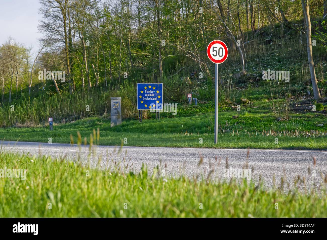 Eine Straßenszene mit einem Geschwindigkeitsbegrenzungsschild von 50 km/h und einem blauen Schild der Europäischen Union, das die Grenze zwischen Deutschland und dänemark, einschließlich Hintergrund, anzeigt Stockfoto