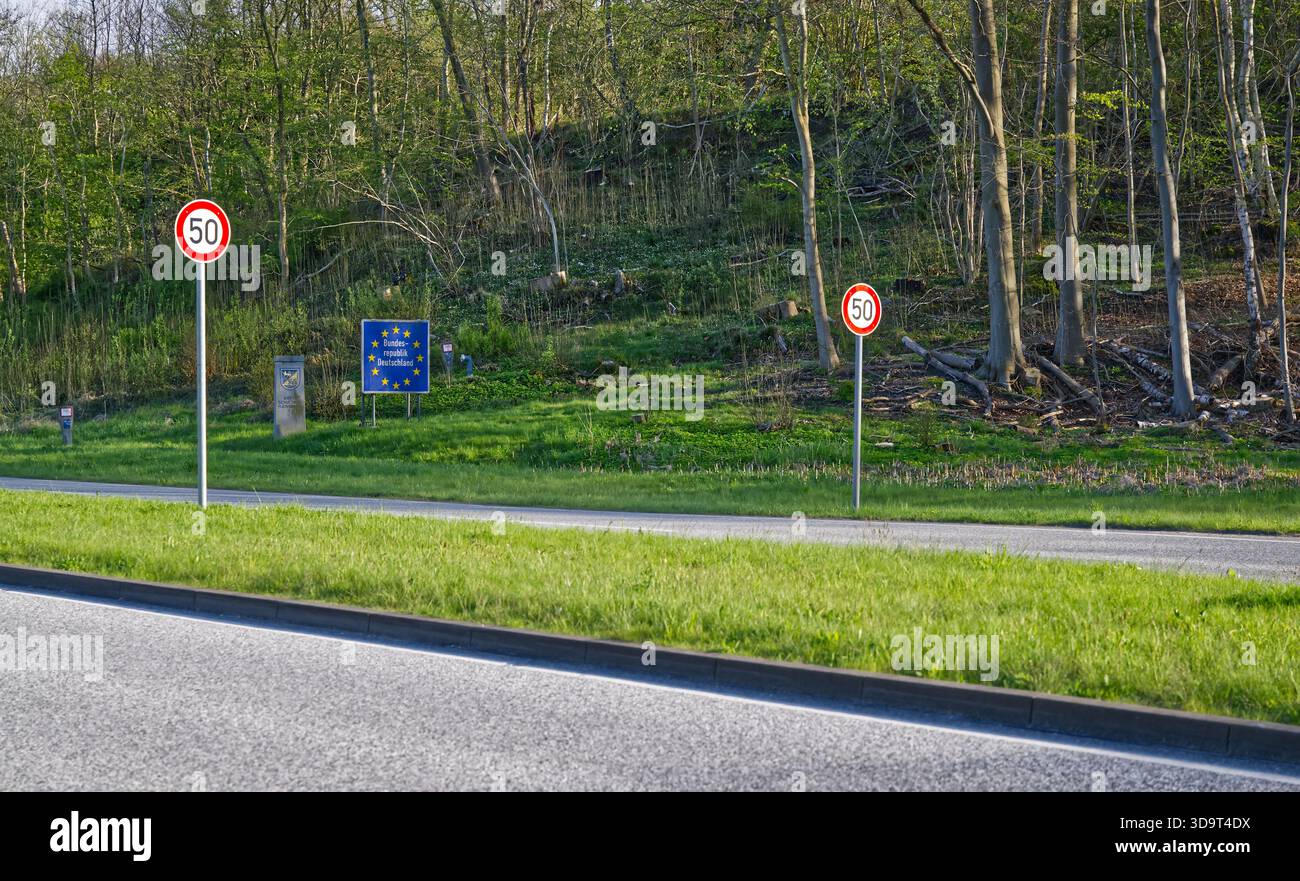 Eine Straßenszene mit einem Geschwindigkeitsbegrenzungsschild von 50 km/h und einem blauen Schild der Europäischen Union, das die Grenze zwischen Deutschland und dänemark, einschließlich Hintergrund, anzeigt Stockfoto