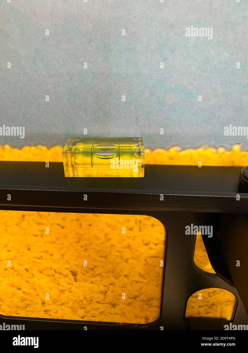 Eine Nahaufnahme einer Wasserwaage auf einem schwarzen Metallrahmen mit gelbem Hintergrund. Der Pegel zeigt eine Blase an, die anzeigt, dass er ausgeglichen ist. Stockfoto