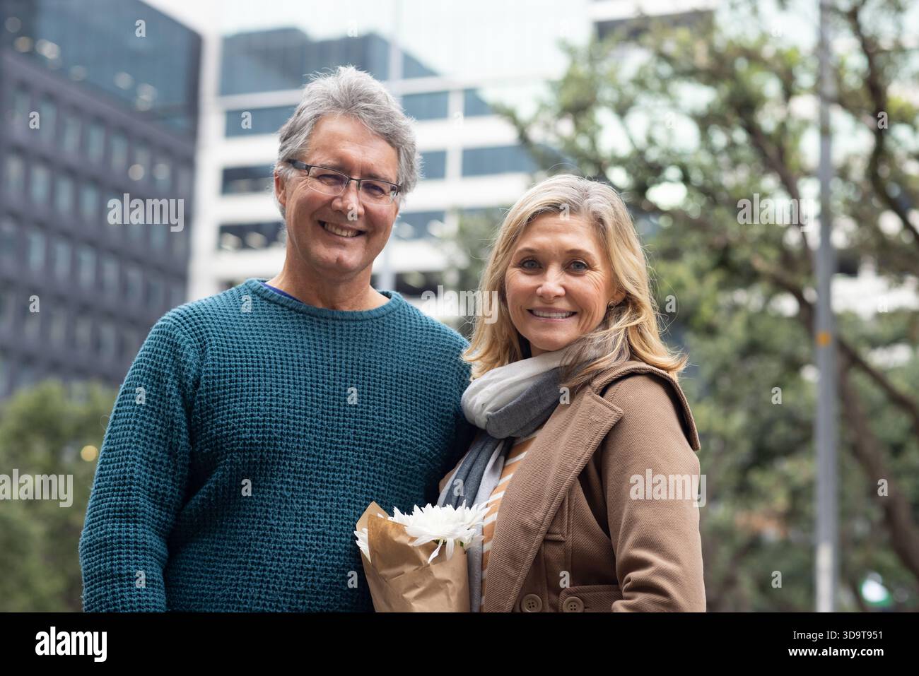 Paare stehen auf dem City plaza in einem blauen Pullover und braunem Mantel mit eingewickeltem weißen Blumenstrauß Stockfoto