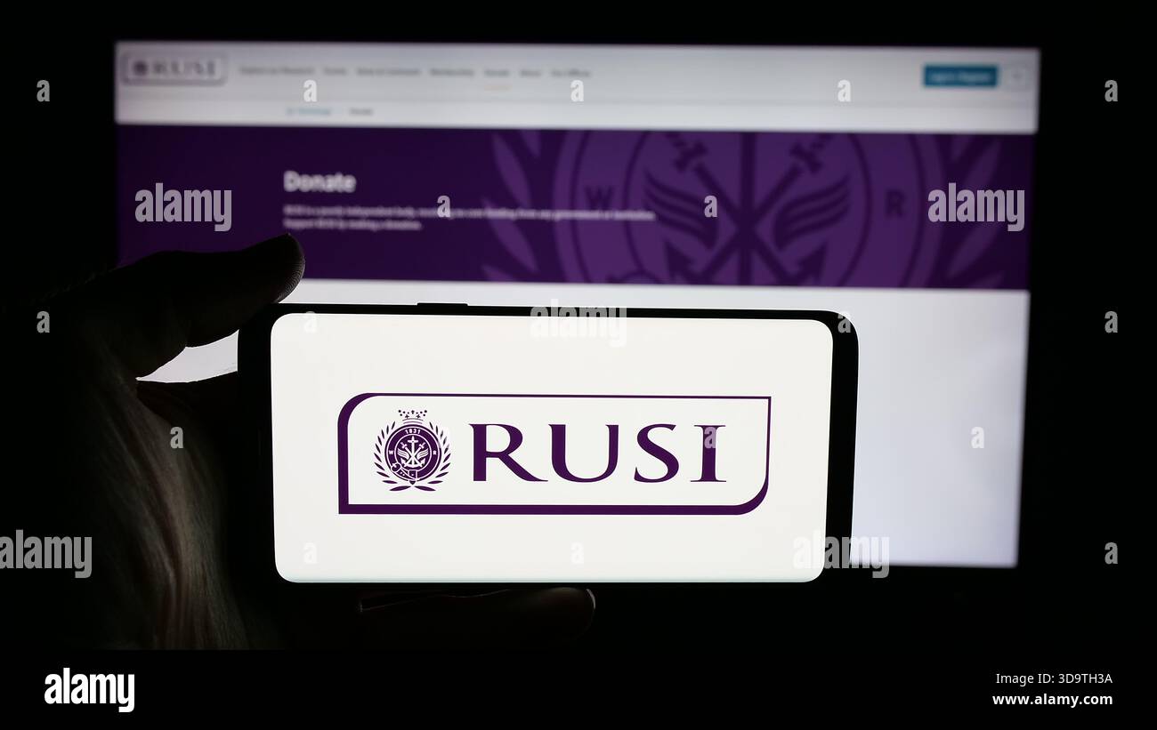 Stuttgart, Deutschland - 24.11.2025: Person, die ein Mobiltelefon mit dem Logo des Royal United Services Institute (RUSI) auf dem Bildschirm vor der Webseite hält. Stockfoto