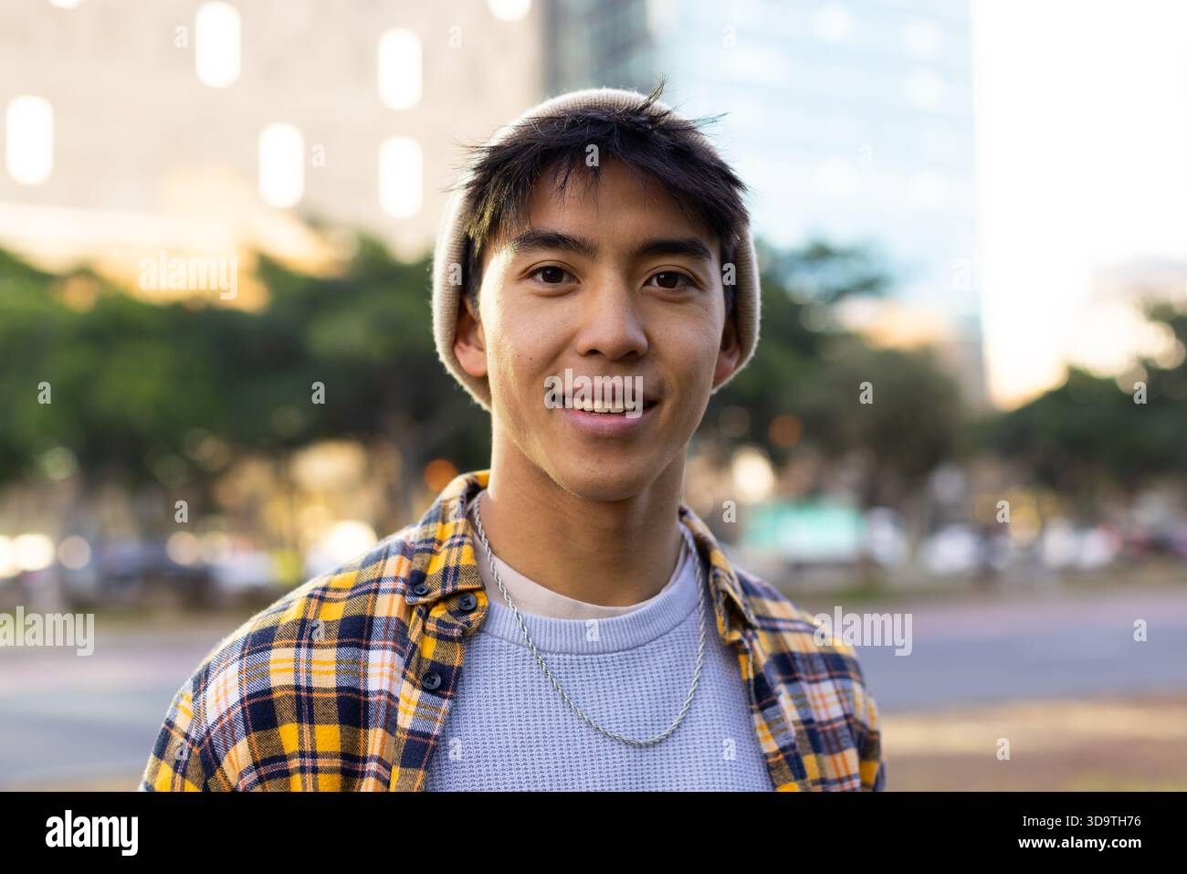 Asiatischer Mann, der nachmittags im Park an der Straße steht, mit beiger Mütze und silberner Kette Stockfoto
