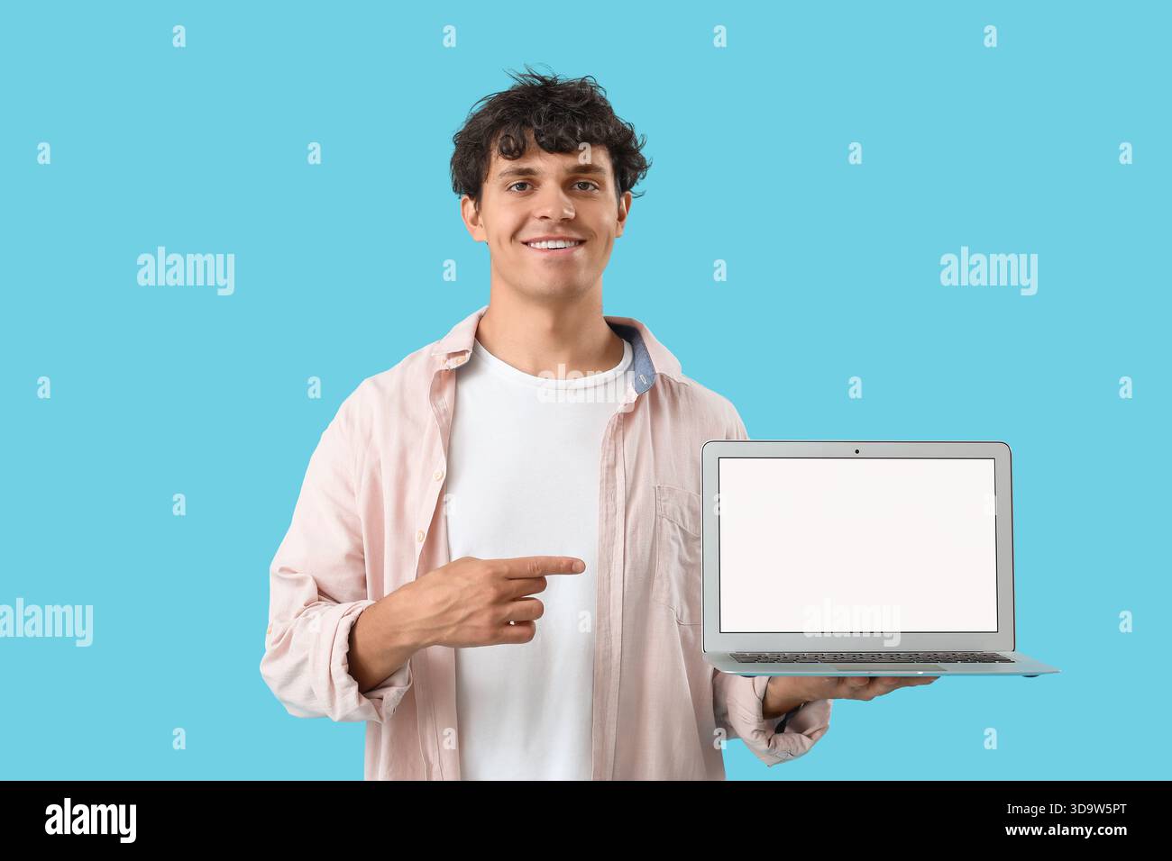 Männlicher Programmierer zeigt auf leeren Laptop auf blauem Hintergrund Stockfoto