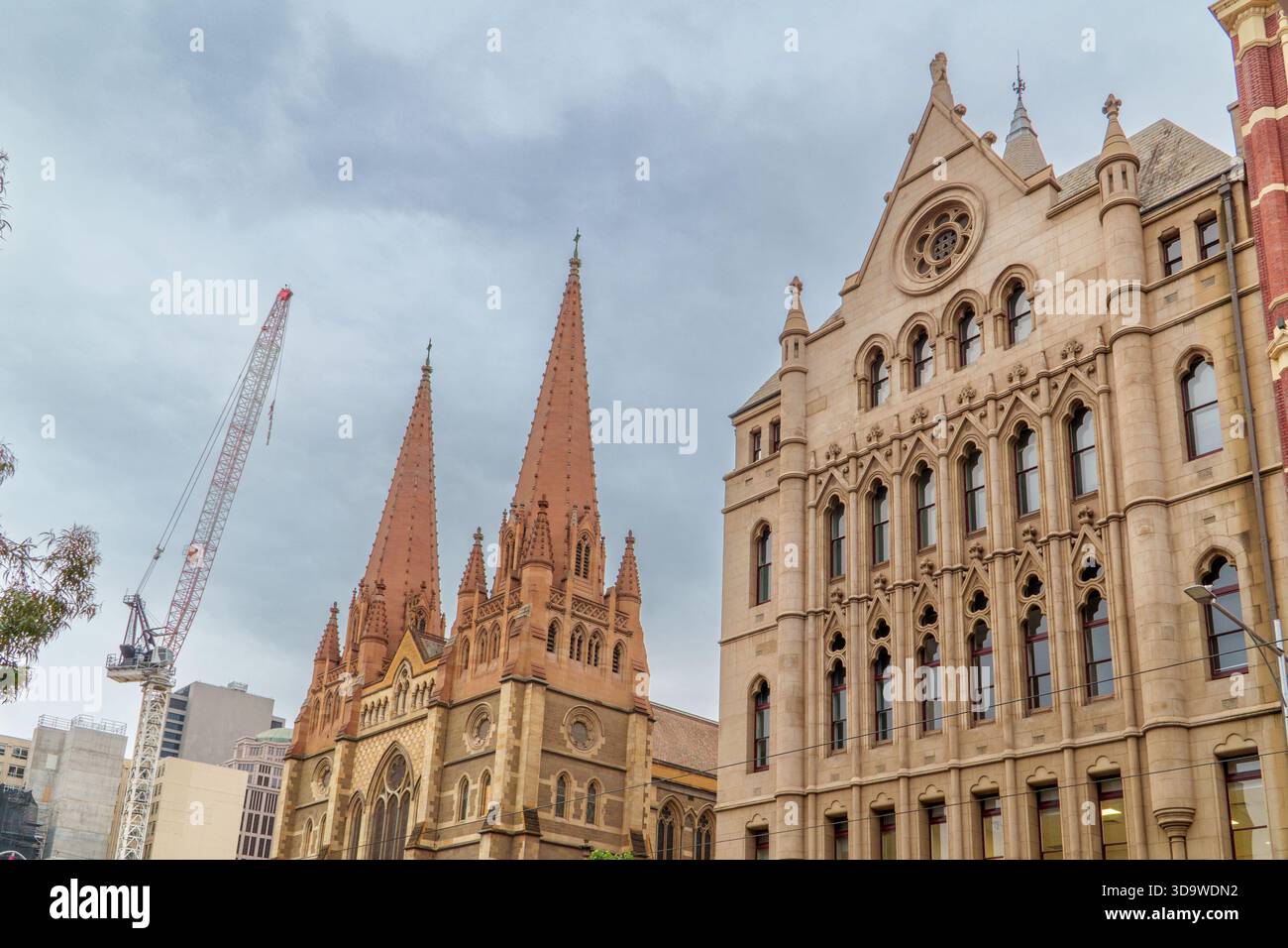 Die Türme der St. Pauls Cathedral und ein reich verziertes Gebäude im gotischen Stil stehen vor einem bewölkten Himmel mit einem hoch aufragenden Baukran in der Nähe. Stockfoto