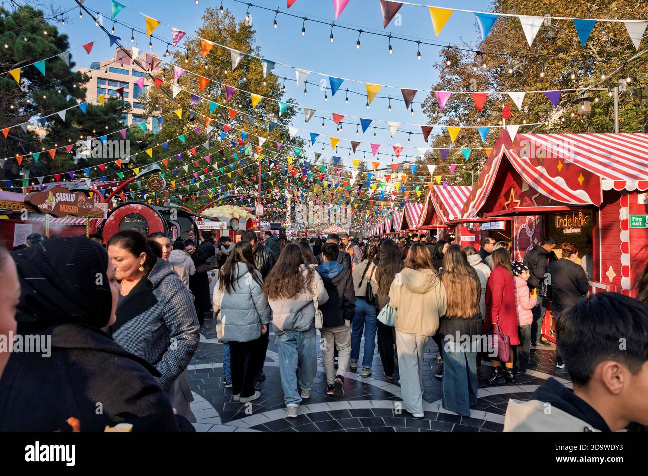 Überfüllter Markt vor dem Neujahr mit farbenfrohen Flaggen, festlichen Ständen und Menschen, die zwischen hellen Weihnachtsdekorationen spazieren gehen. Stockfoto