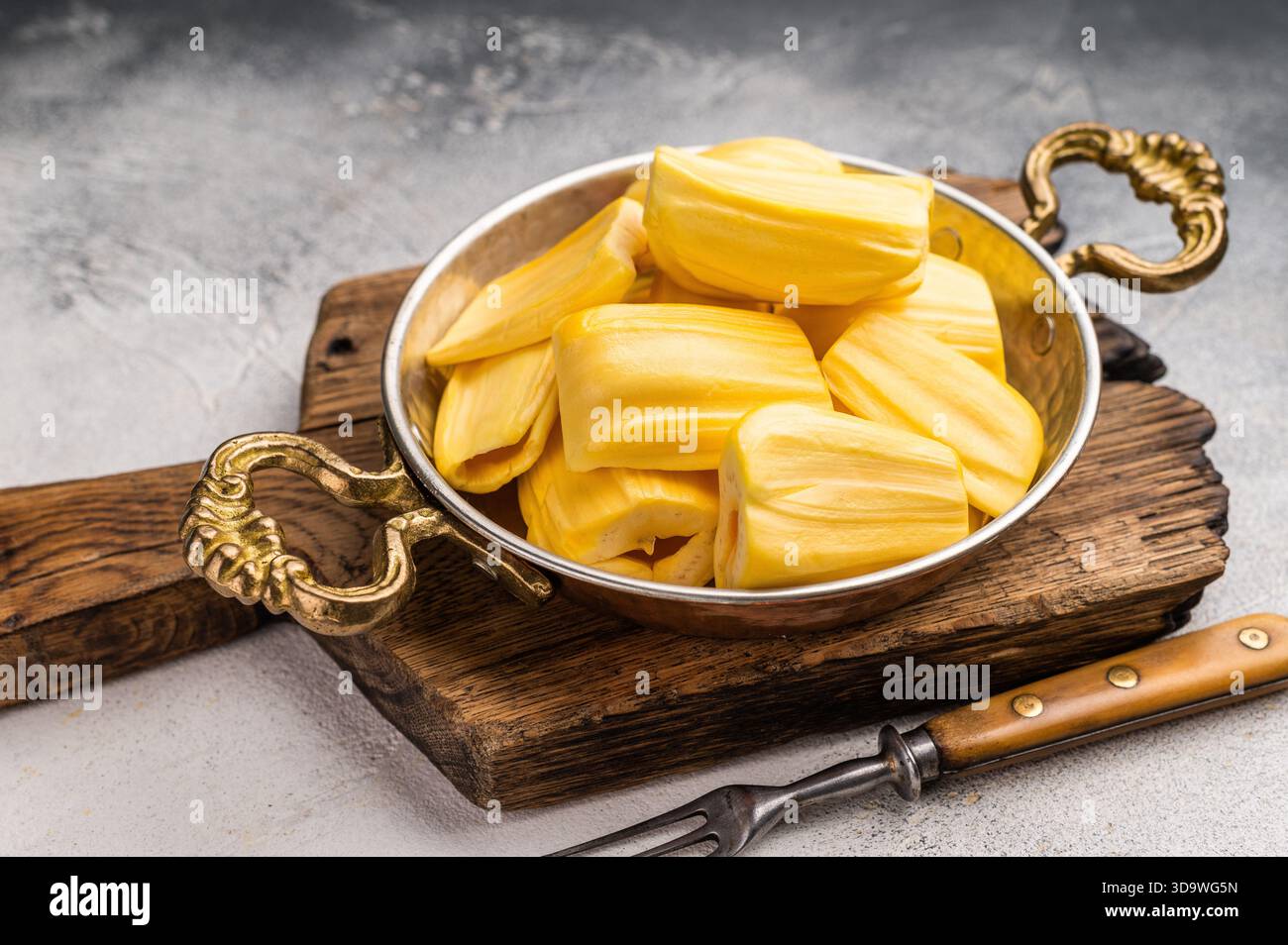 Süße, goldene Jackfrucht-Schoten (Zwiebeln) in einer traditionellen Metallschale mit Gabel. Exotischer tropischer Snack oder Dessert mit Kopierraum. Stockfoto