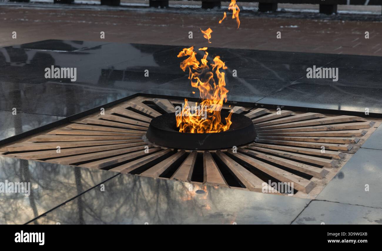 Eine symbolische Gedenkstätte für ewige Flammen in einer kreisförmigen Struktur mit reflektierenden Oberflächen und einem lebendigen Feuer, das Erinnerung und Ehre repräsentiert Stockfoto
