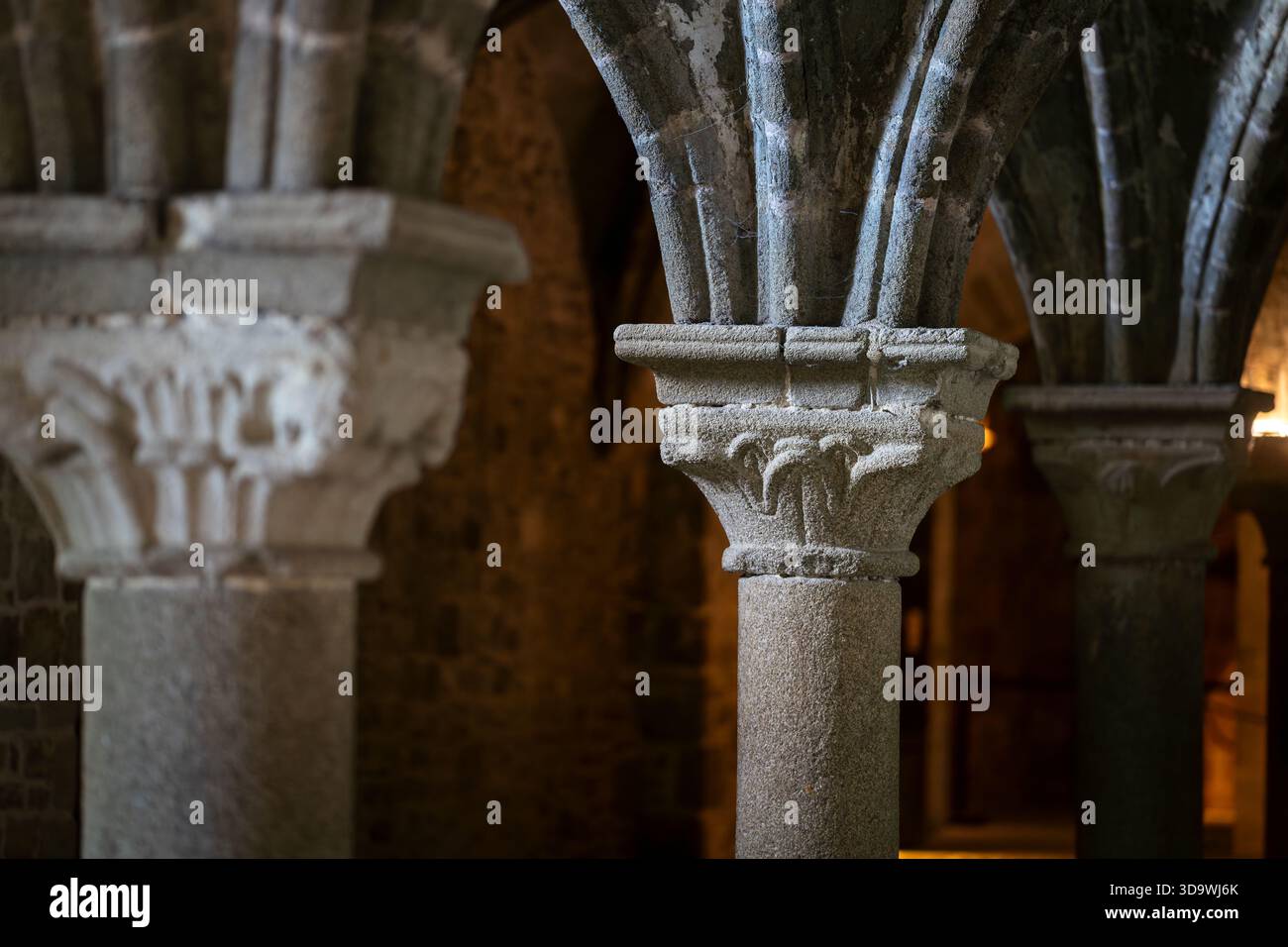 Steinsäulen und geschnitzte Kapitelle im gotischen Inneren der Abtei Mont-Saint-Michel. Historische Gewölbearchitektur mit detaillierten Steinkapitellen. Stockfoto
