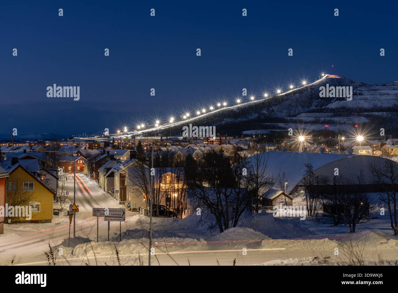 Kiruna, Schweden, nachts im Winter, mit der Skipiste im Hintergrund, warmen Straßenlichtern und Blautönen am Himmel Stockfoto