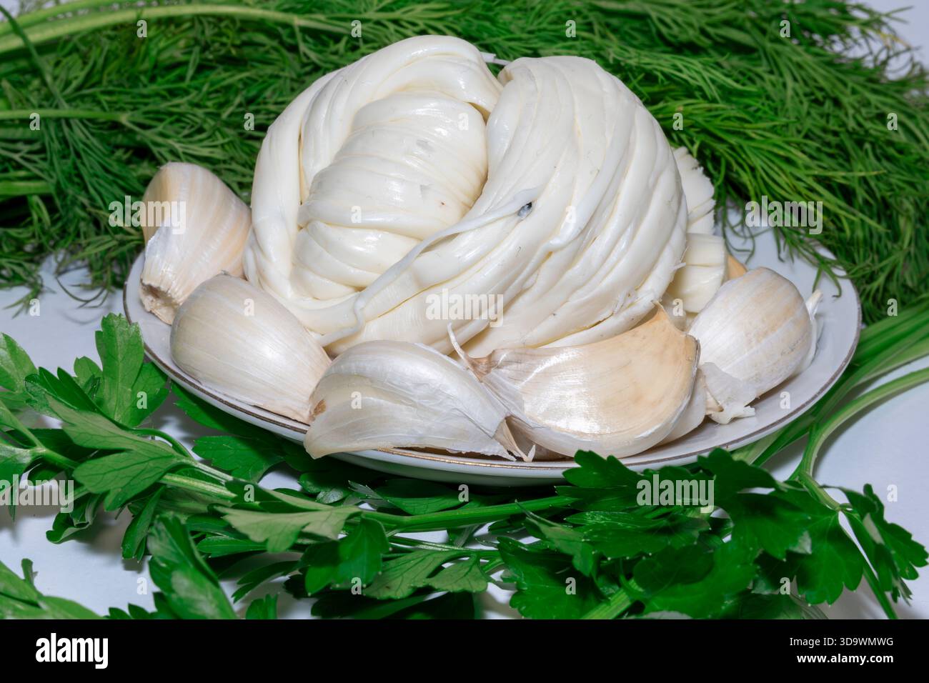 Geflochtener kaukasischer Chechil-Käse, Knoblauch und frische Kräuter. Ein traditioneller Appetit Stockfoto