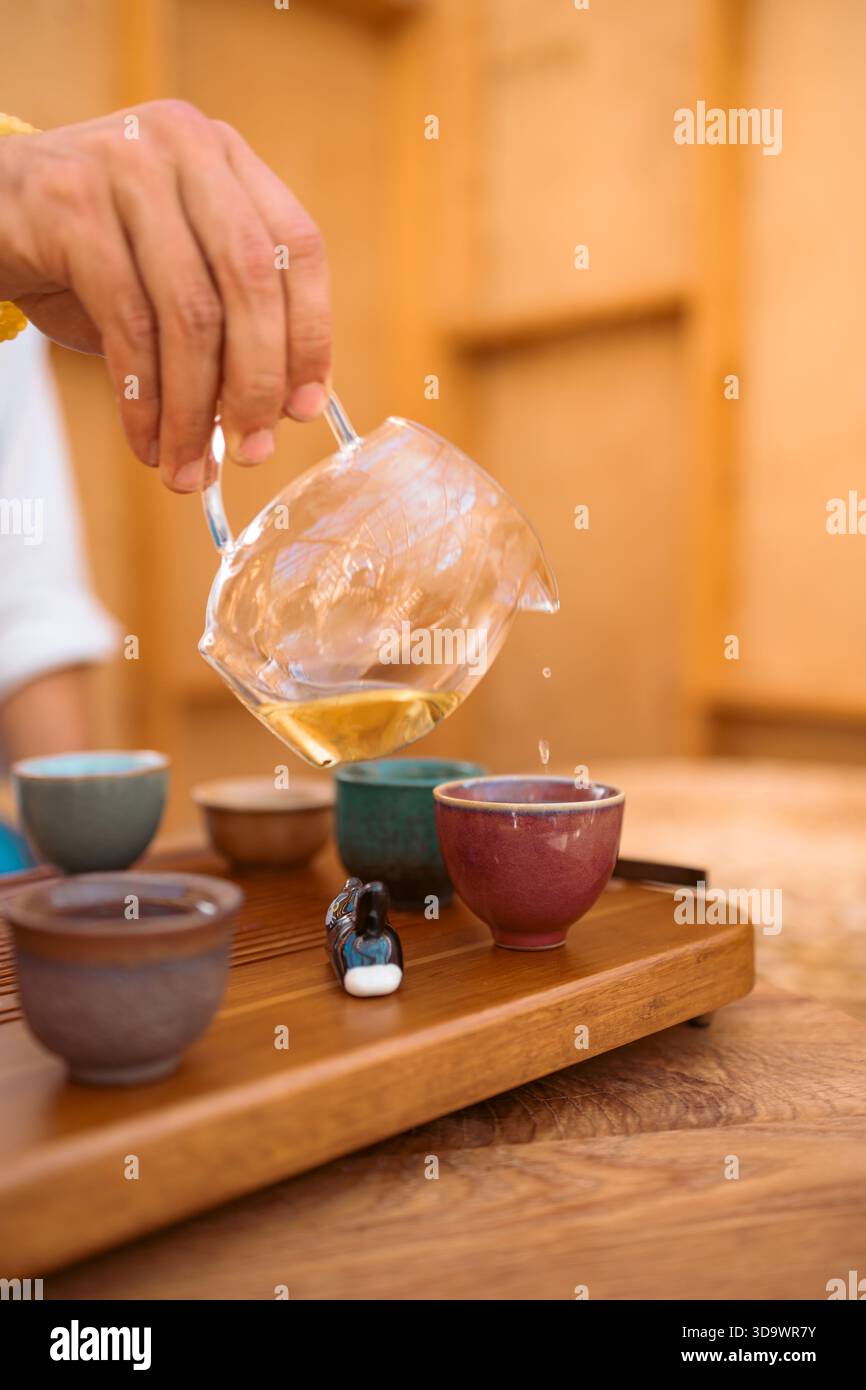 Nahaufnahme einer traditionellen chinesischen Gongfu-Teezeremonie. Ein Fluss duftenden Oolong-Tees wird aus einer Tonkanne Yixing in eine einfache Keramik gegossen Stockfoto