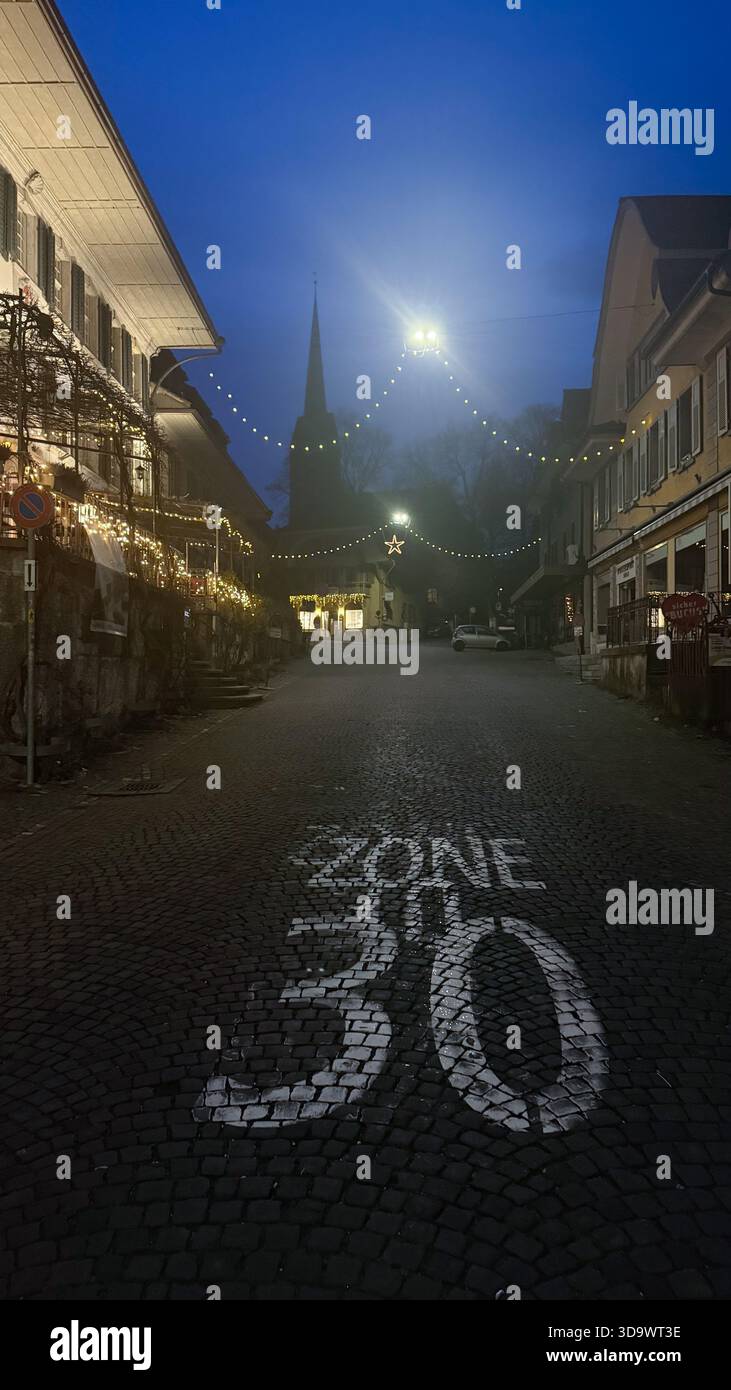 Nächtliche Straßenszene mit Geschwindigkeitsmarkierung der Zone 30 auf dem Bürgersteig, warmen Lichtern, historischen Gebäuden und ruhiger urbaner Atmosphäre in abendlicher Atmosphäre Stockfoto