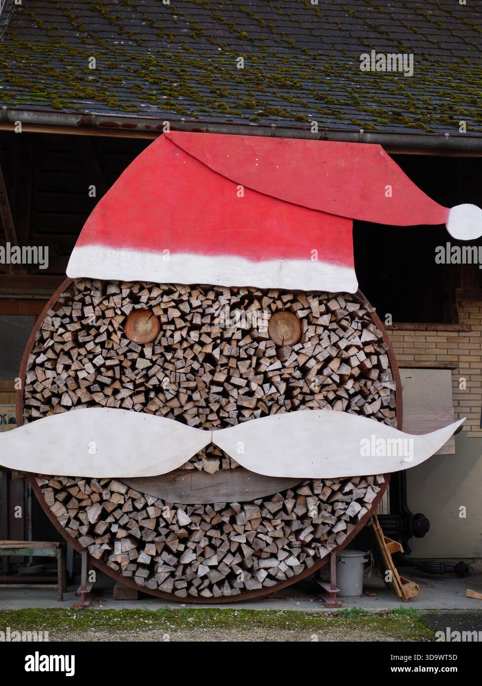 Kreative Holzlagerstruktur, dekoriert als Weihnachtsmann mit Rothut, weißem Schnurrbart und kreisförmigem Baumstamm-Muster außerhalb der rustikalen Scheune. Hochwertige Fotos Stockfoto