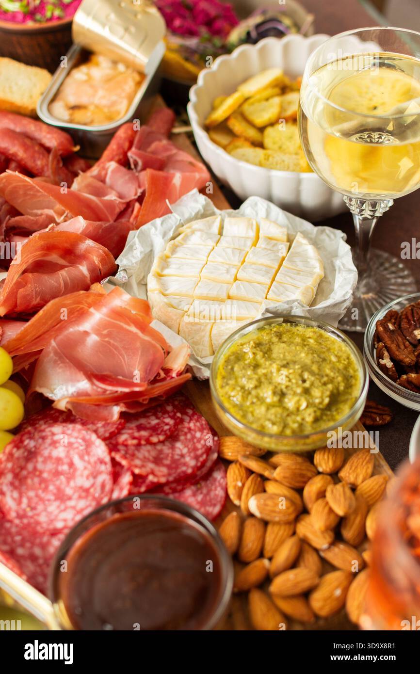 Versammelt um eine wunderschön gestaltete Wurstplatte gefüllt mit verschiedenen Käsesorten, köstlichen Würstchen, cremigem Hummus und frischen Trauben. Perfekt für Stockfoto