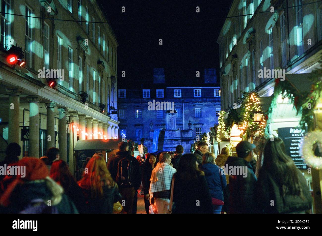 Bath, England - 3. Dezember 2025: Bath Christmas Market, mit Verkaufsständen, Verkaufsständen und Käufern. Aufgenommen nach Einbruch der Dunkelheit auf Spezialfilm. Stockfoto