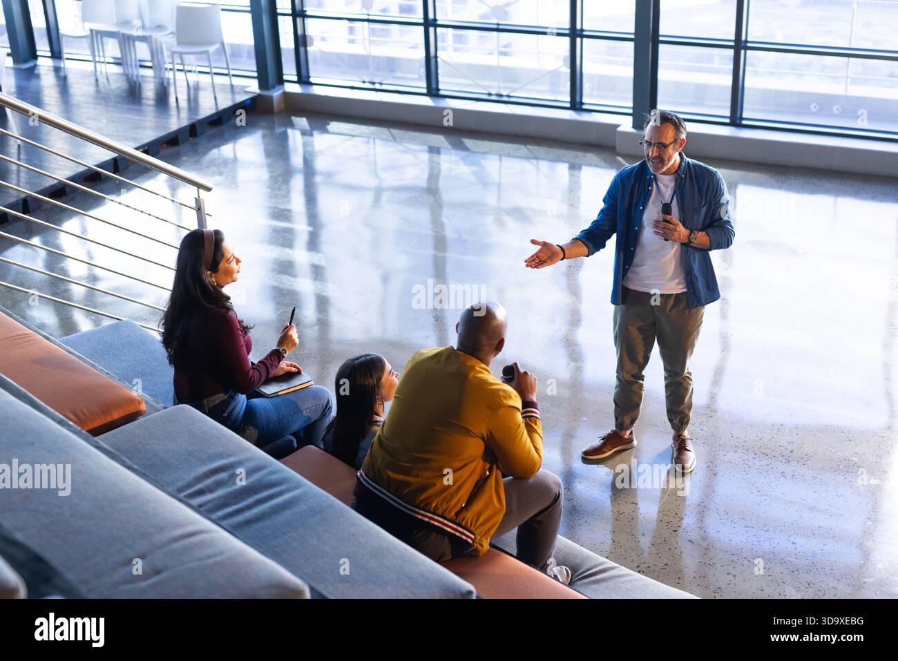 Verschiedene Kollegen, die einen Reisebecher halten, hören den Referenten mit dem Headset-Mikrofon in der Lounge und im Kopierbereich Stockfoto