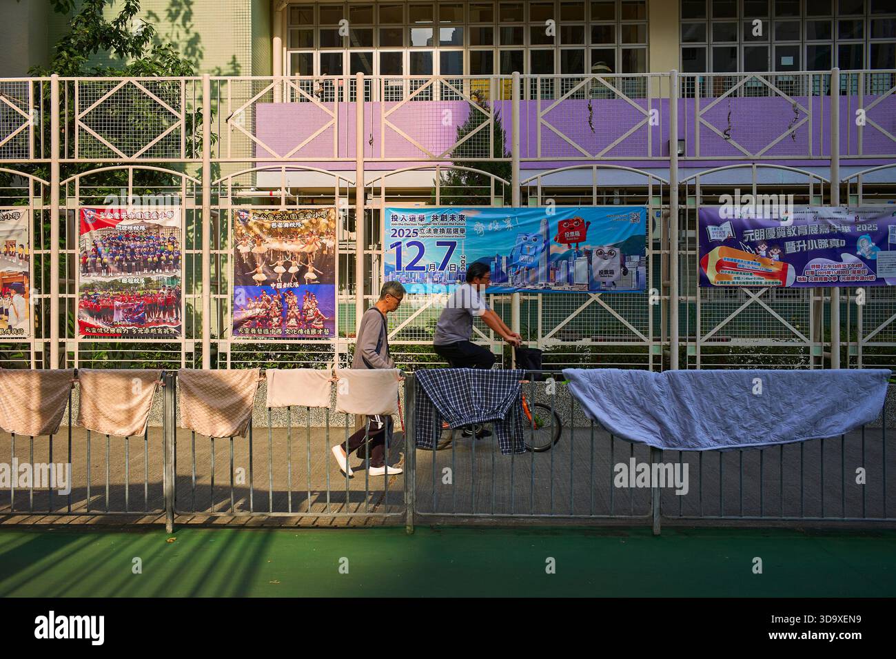 Hongkong, China. Dezember 2025. Ein Mann läuft vorbei und der andere fährt mit dem Fahrrad an einer Schule vorbei, in der sich ein Wahllokal in Tin Shui Wai befindet. Die Parlamentswahlen 2025 in Hongkong finden am 7. Dezember 2025 statt, um die 90 Mitglieder des 8. Hongkonger Legislativrates zu wählen. Quelle: SOPA Images Limited/Alamy Live News Stockfoto