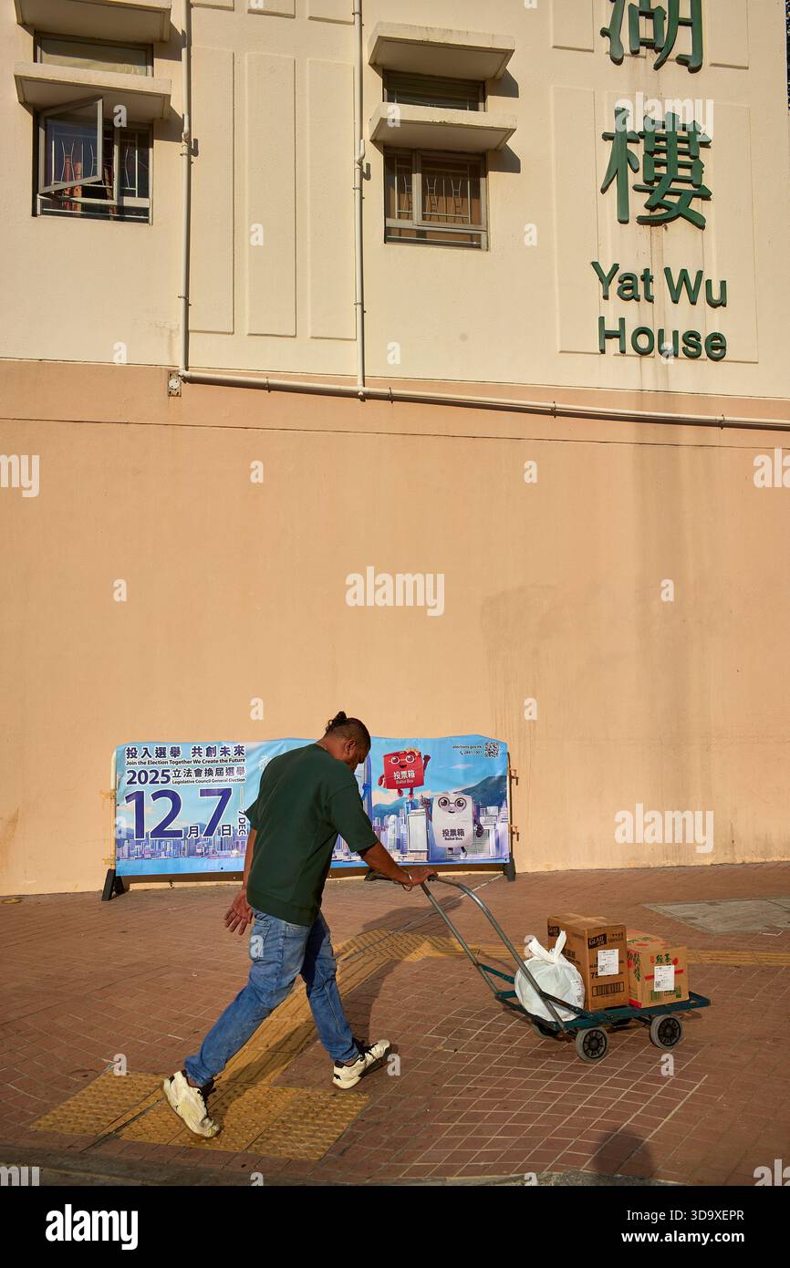 Hongkong, China. Dezember 2025. Ein Liefermann kommt an einem Poster vorbei, auf dem die Leute dazu drängen, in Tin Shui Wai zu wählen. Die Parlamentswahlen 2025 in Hongkong finden am 7. Dezember 2025 statt, um die 90 Mitglieder des 8. Hongkonger Legislativrates zu wählen. Quelle: SOPA Images Limited/Alamy Live News Stockfoto